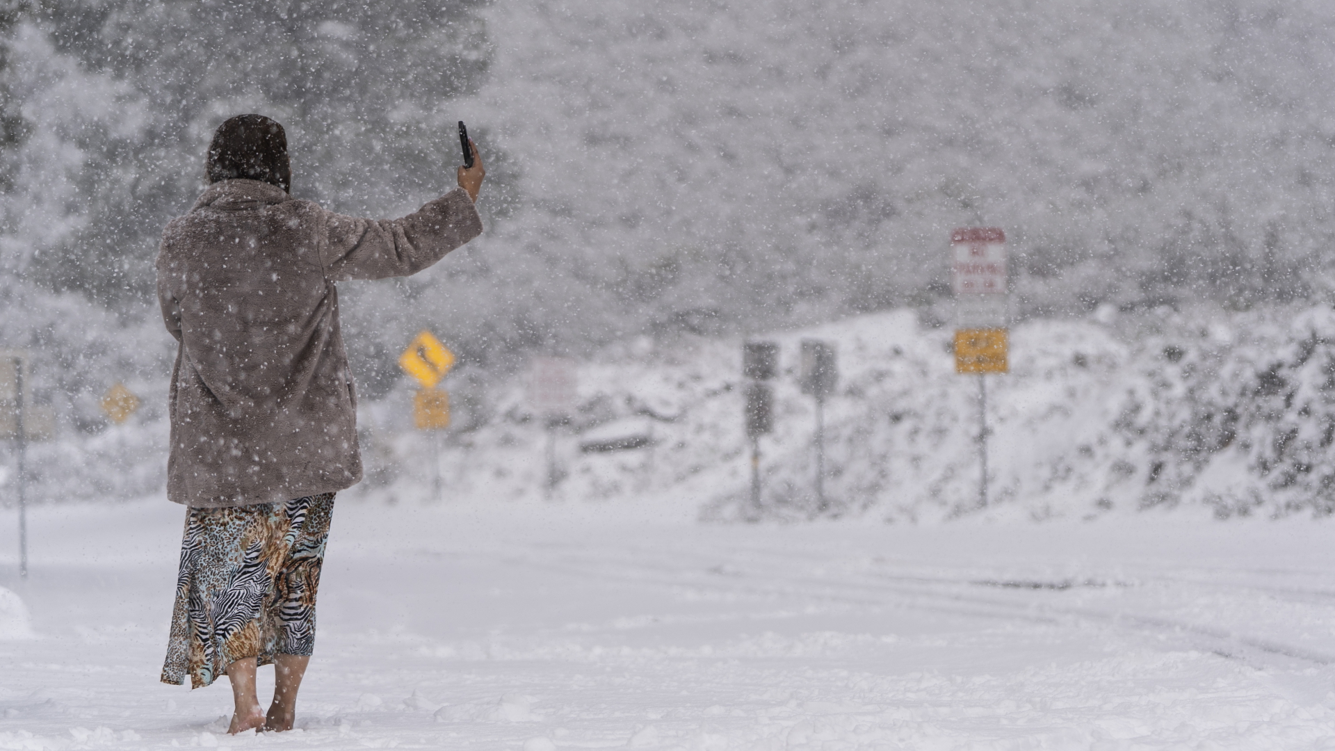 Eine Frau steht auf einer schneebedeckten Straße und macht ein Selfie im Angeles National Forest | dpa