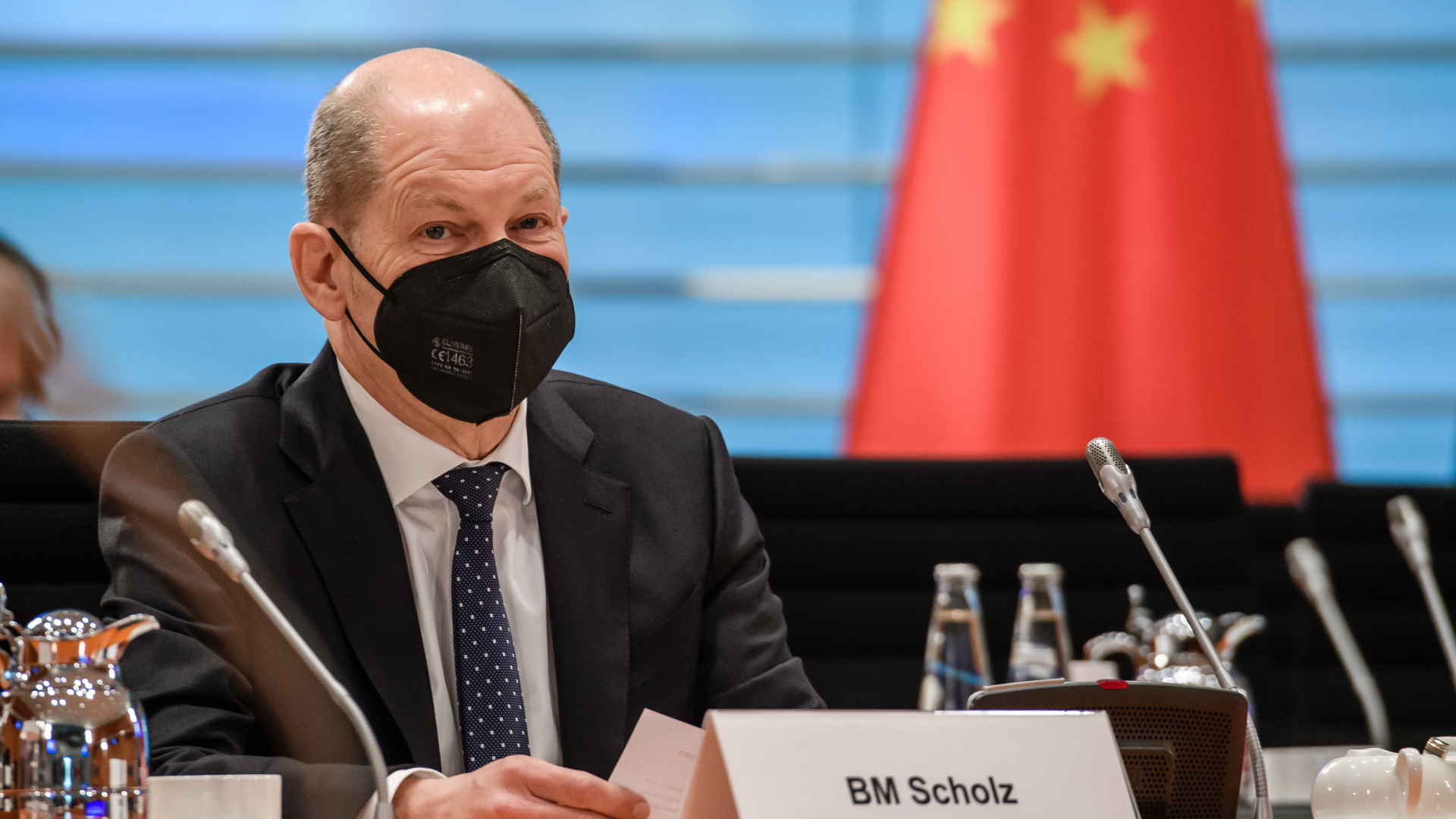 Olaf Scholz sitzt mit FFP2-Maske am Verhandlungstisch, im Hintergrund die Flagge der Volksrepublik China | Bildquelle: EPA