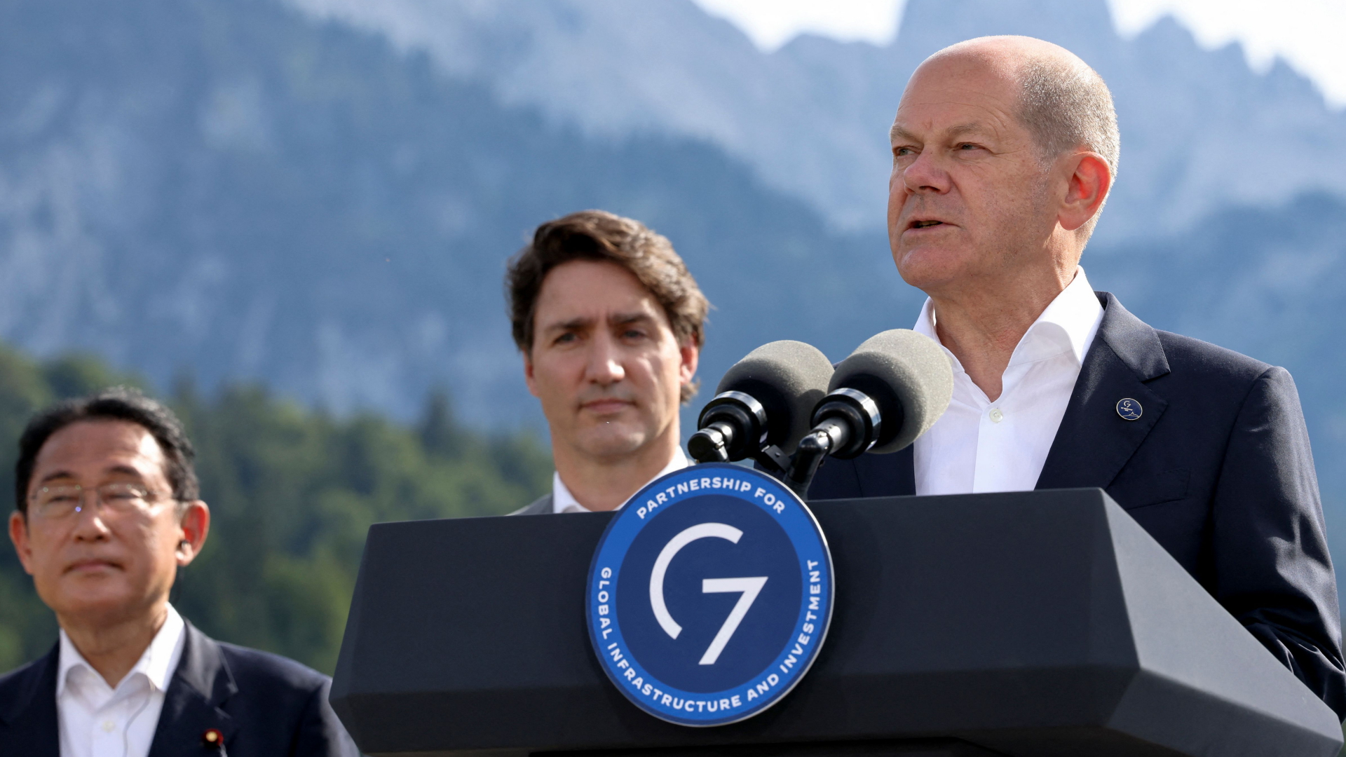 Olaf Scholz spricht beim G7-Gipfel - im Hintergrund Kanadas Premierminister Justin Trudeau und Japans Premier Fumio Kishida | AFP