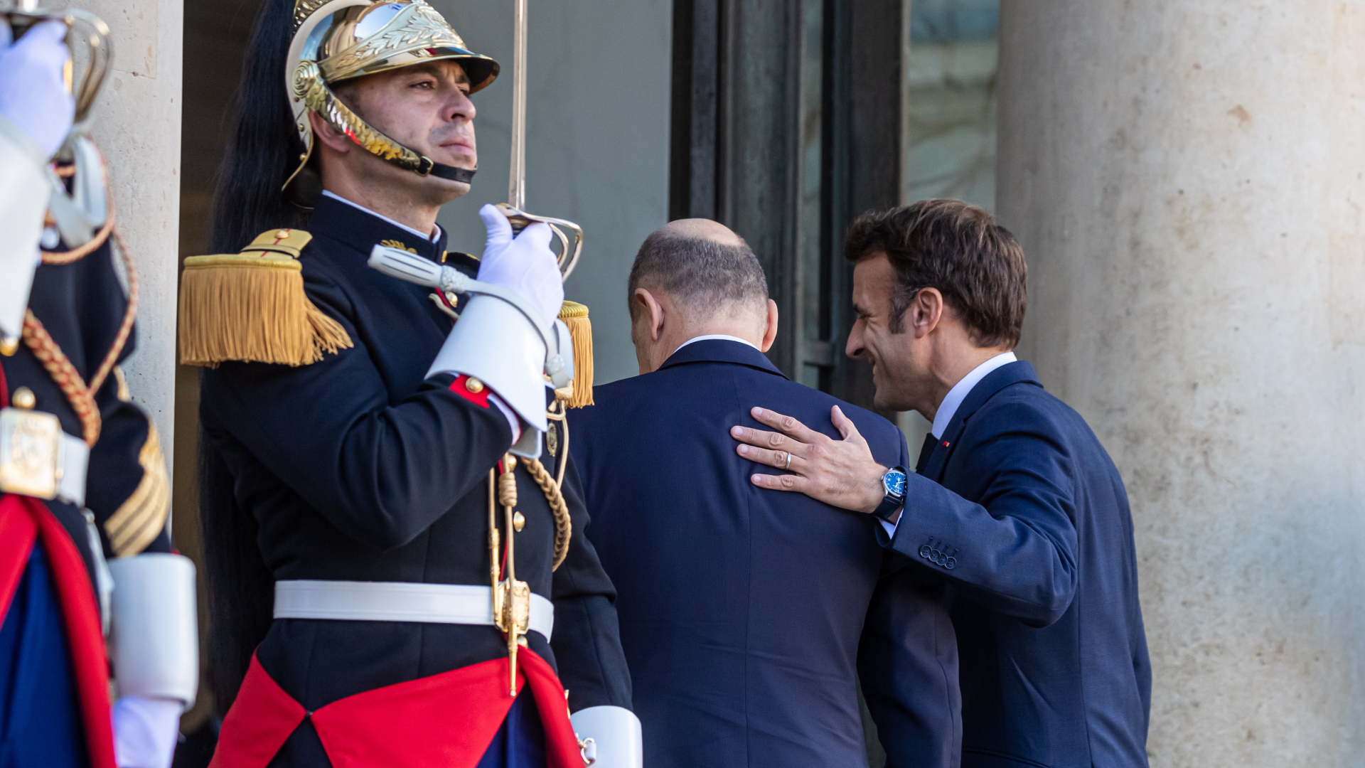 Emmanuel Macron legt Olaf Scholz eine Hand auf den Rücken, während sie an Wachen vorbei in den Elysée-Palast gehen.  | EPA