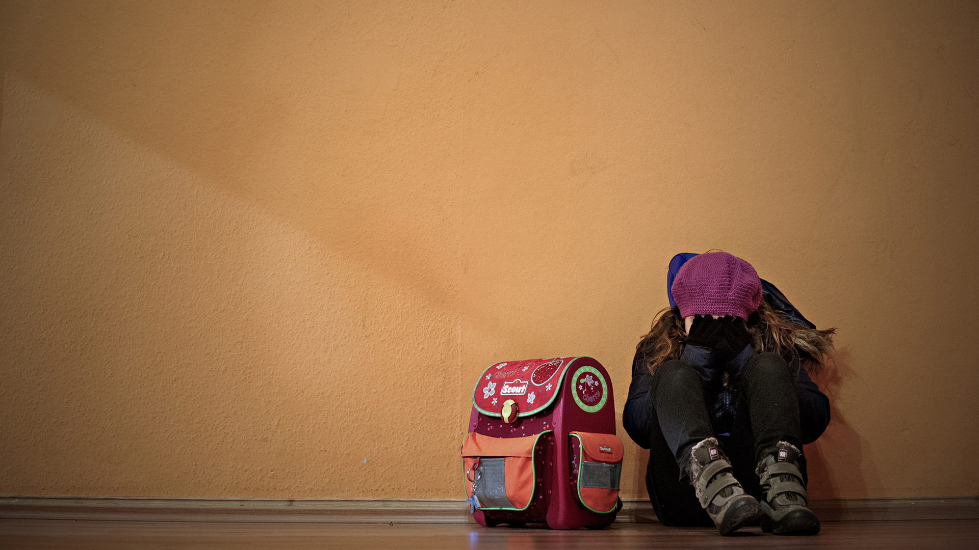 Ein Mädchen sitzt neben ihrem Schulranzen auf dem Boden und hält die Hände vor das Gesicht. | dpa
