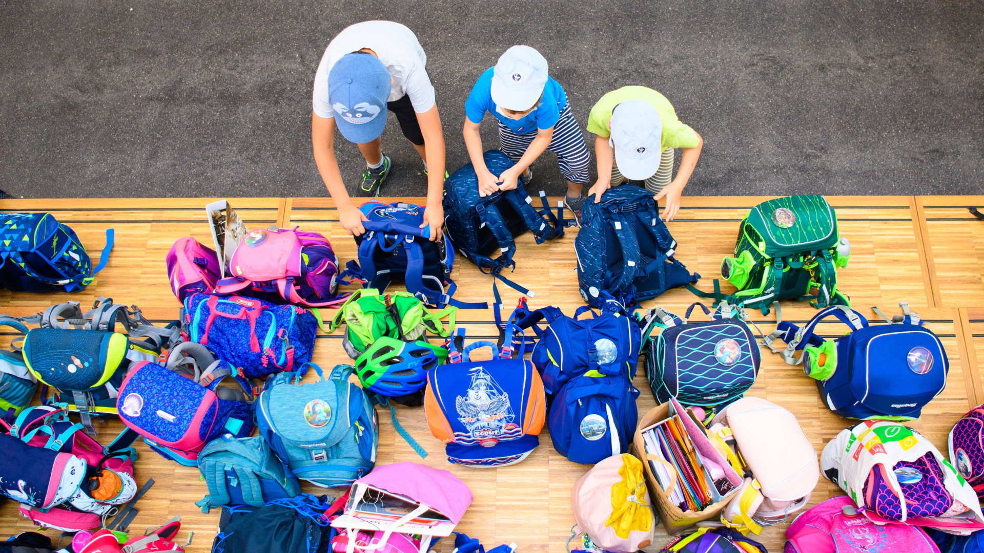 Drei Erstklässler stellen in einer Grundschule auf einem Podest ihre Schultaschen ab. | dpa