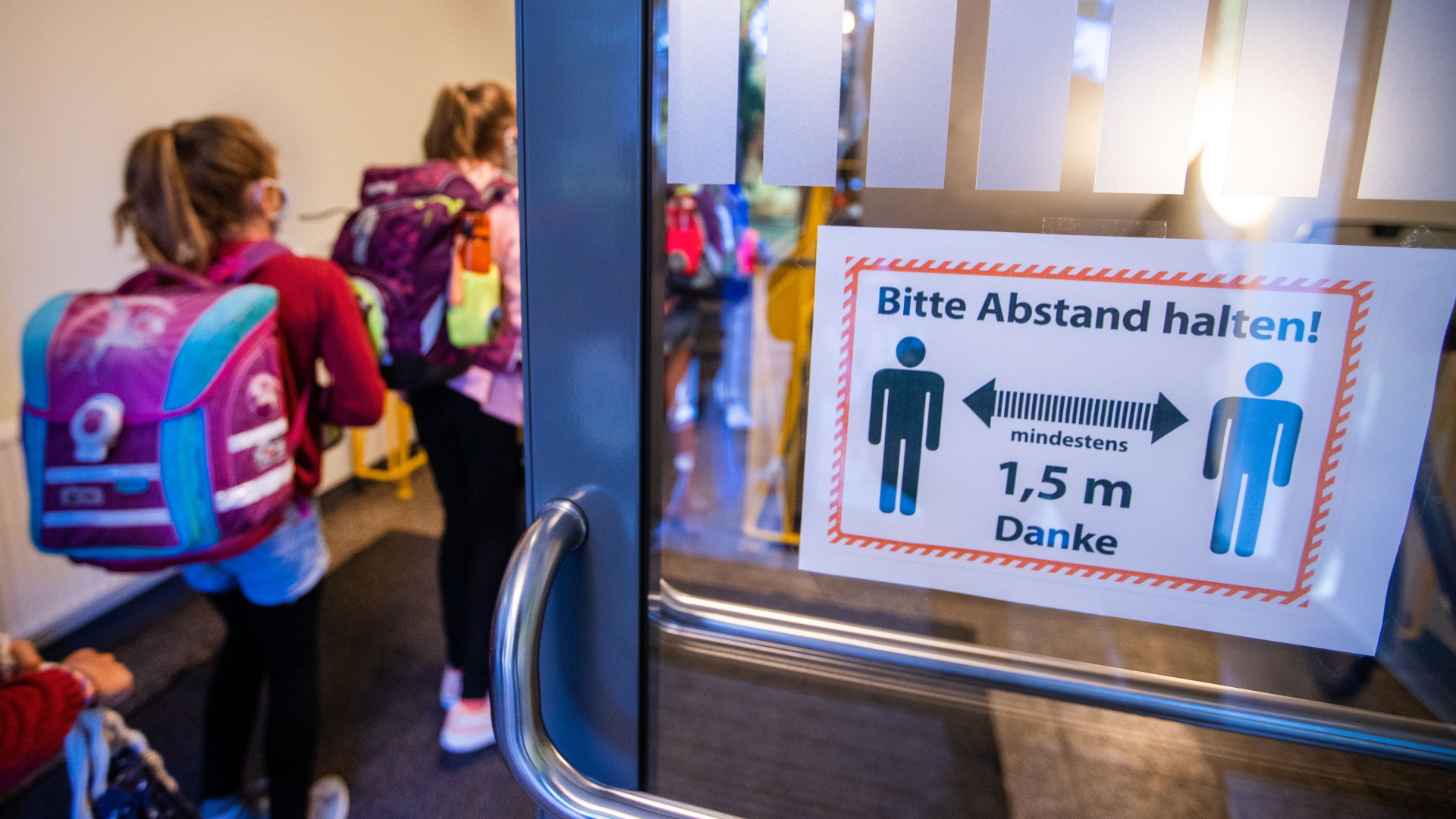 Schwerin: Schüler gehen am ersten Schultag nach den Sommerferien durch einen Eingang mit einem Hinweisschild zu den Sicherheitsabständen als Corona-Schutzmaßnahme zu ihrem Klassenraum.