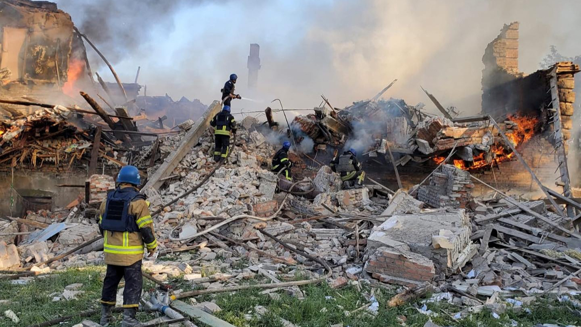 Die Einsatzkräfte kümmern sich um ein Feuer in der Nähe brennender Trümmer, nachdem im Dorf Bilogriwka ein Schulgebäude durch Beschuss getroffen worden war. | via REUTERS