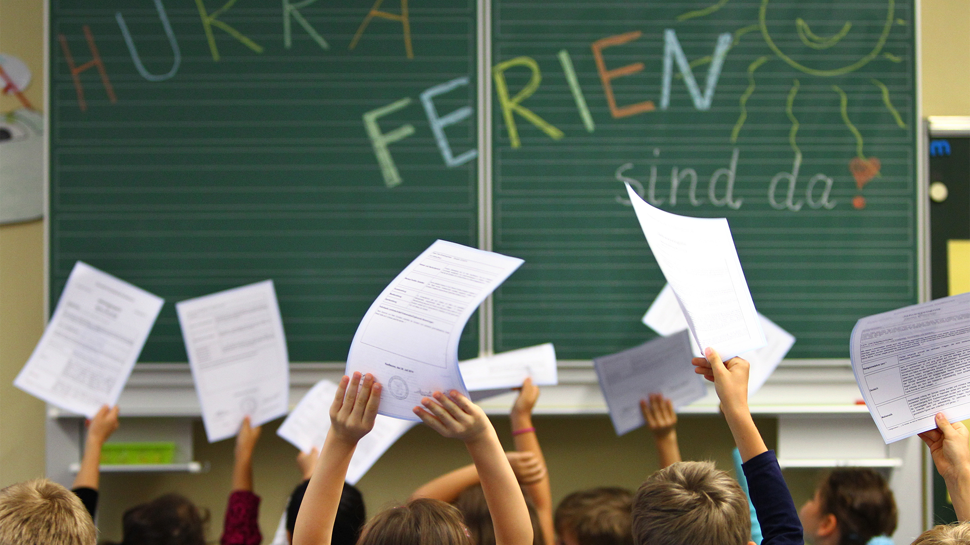 Schüler einer ersten Klasse halten ihre Zeugnisse vor einer Tafel mit der Aufschrift ''Hurra Ferien sind da'' | picture alliance / Karl-Josef Hi