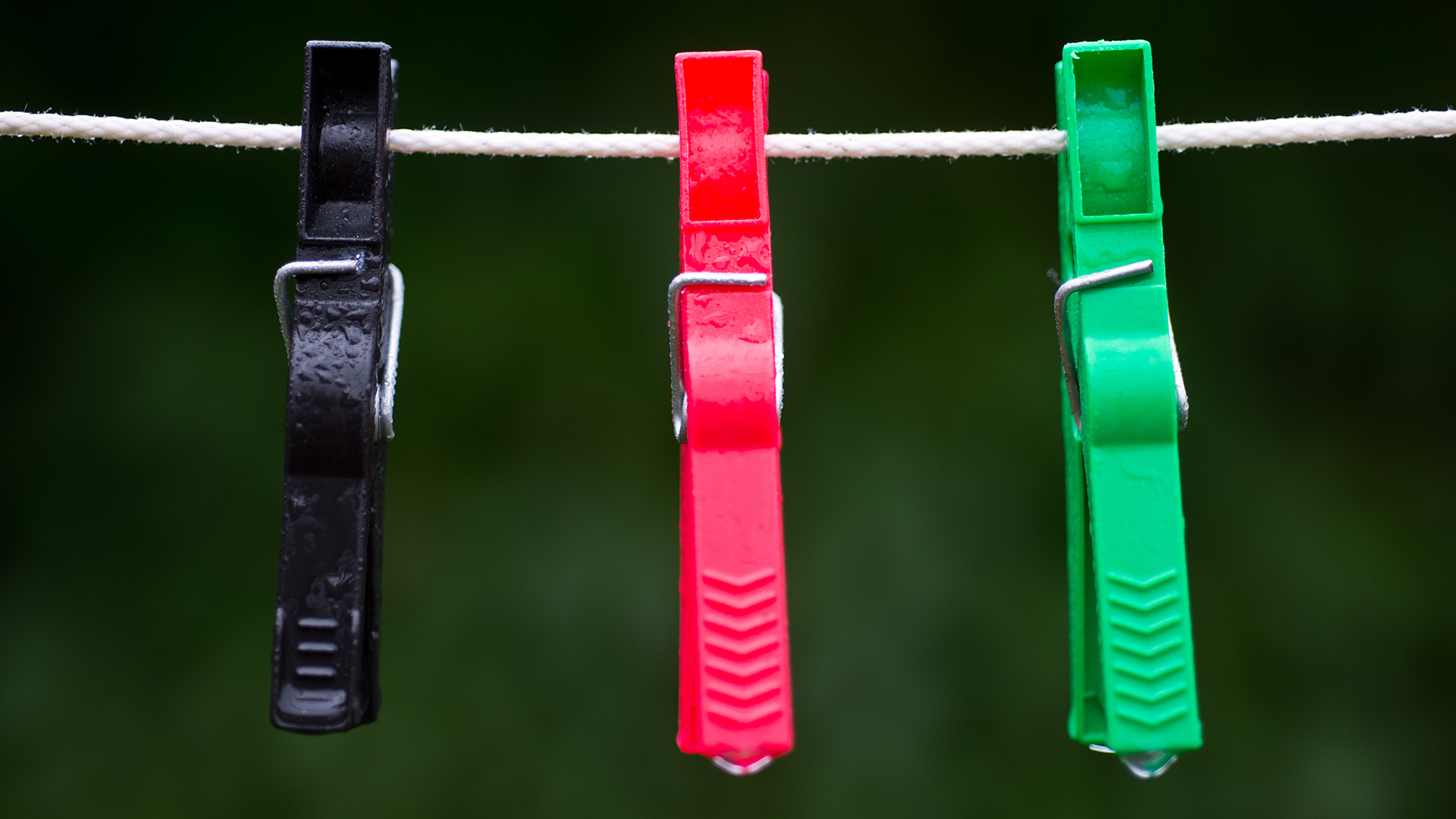 Wäscheklammern in den Farben schwarz, rot und grün hängen im Regen an einer Wäscheleine. | picture alliance / dpa