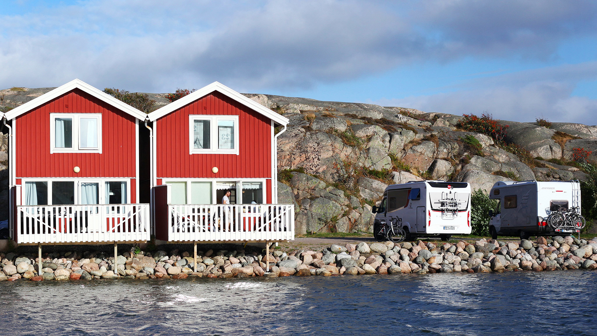 Rote Schwedenhäuschen aus Holz stehen am Wasser auf einem Campingplatz in der Nähe von Kungsham an der Westküste von  Schweden. Daneben stehen Caravans. | picture alliance / Wolfram Stein