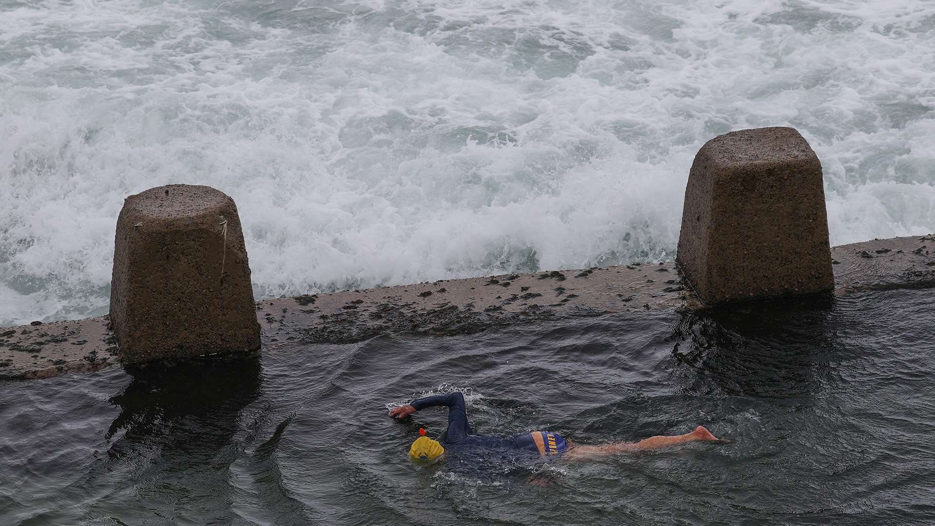Eine Person schwimmt in einem Felsenbecken, während große Wellen an den Coogee Beach in Sydney (Australien) treffen. | REUTERS