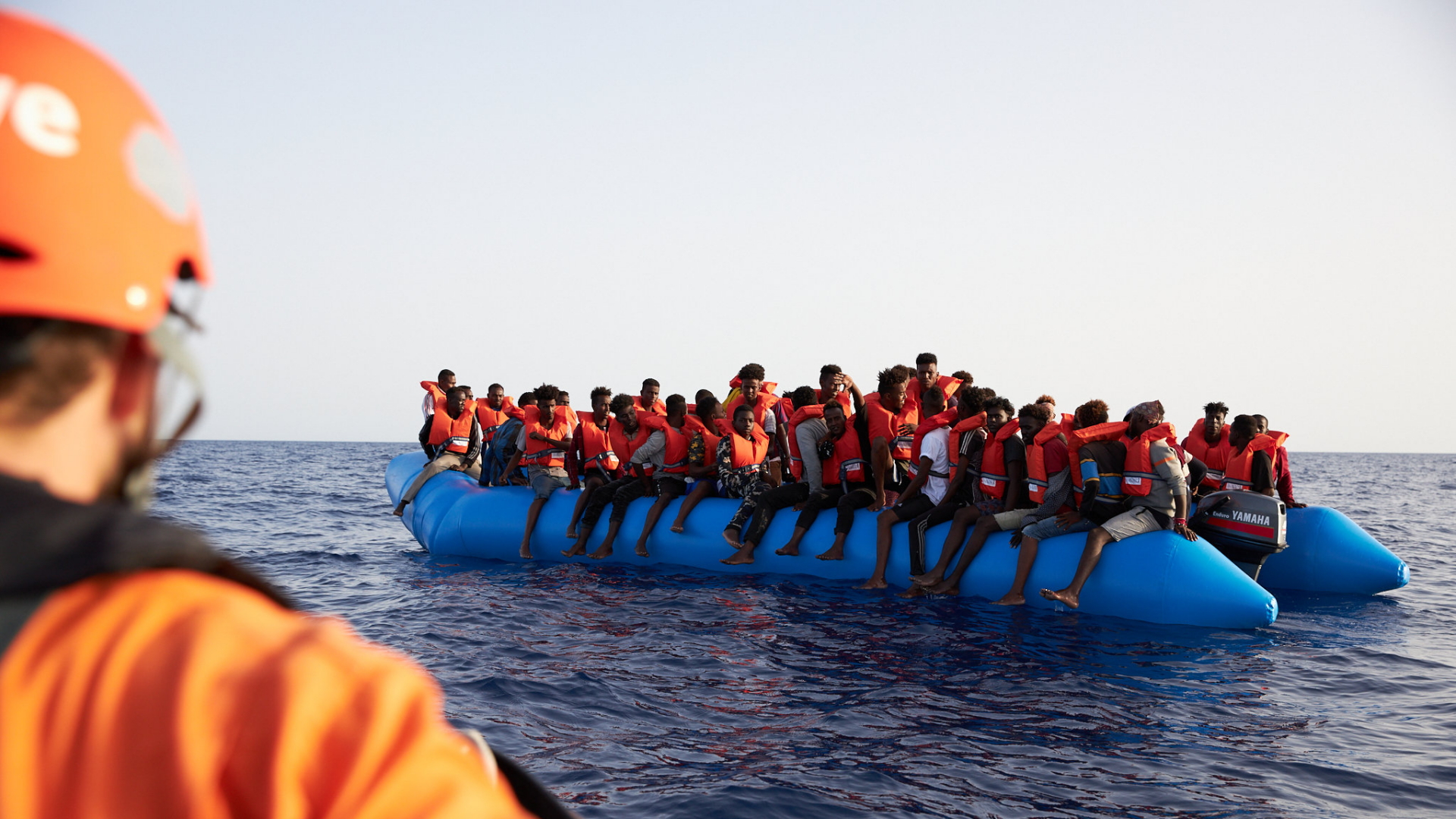 Die von der Seenotrettungsorganisation Sea-Eye herausgegebene Aufnahme zeigt einen Seenotretter (l) der zu einem Flüchtlingsboot schaut.  | dpa