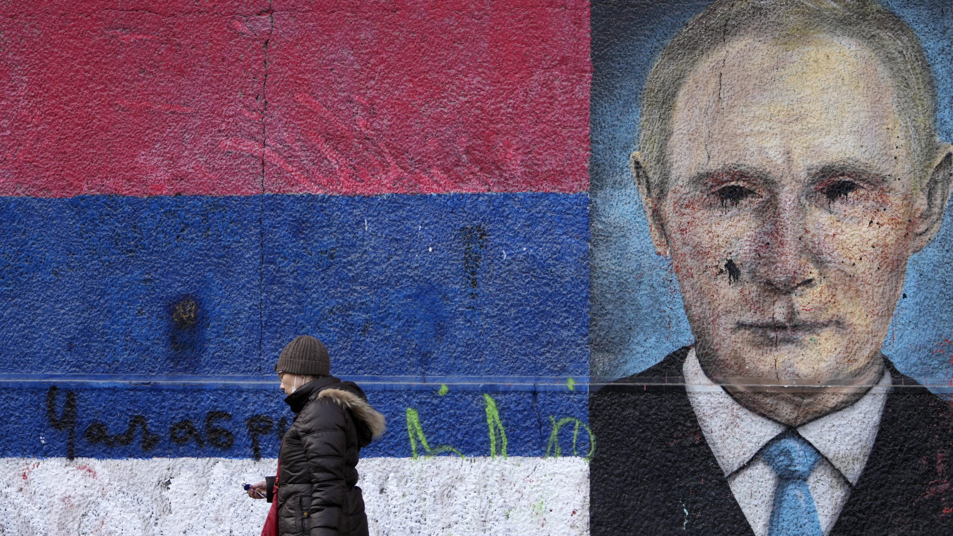 Eine Frau geht in Belgrad an einem Graffiti vorbei, das den russischen Präsidenten Wladimir Putin neben den Farben der serbischen Flagge zeigt. | AP
