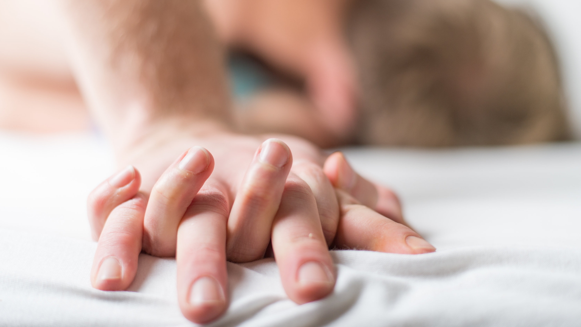 Ein junges Paar liegt im Bett und hält die Hände.