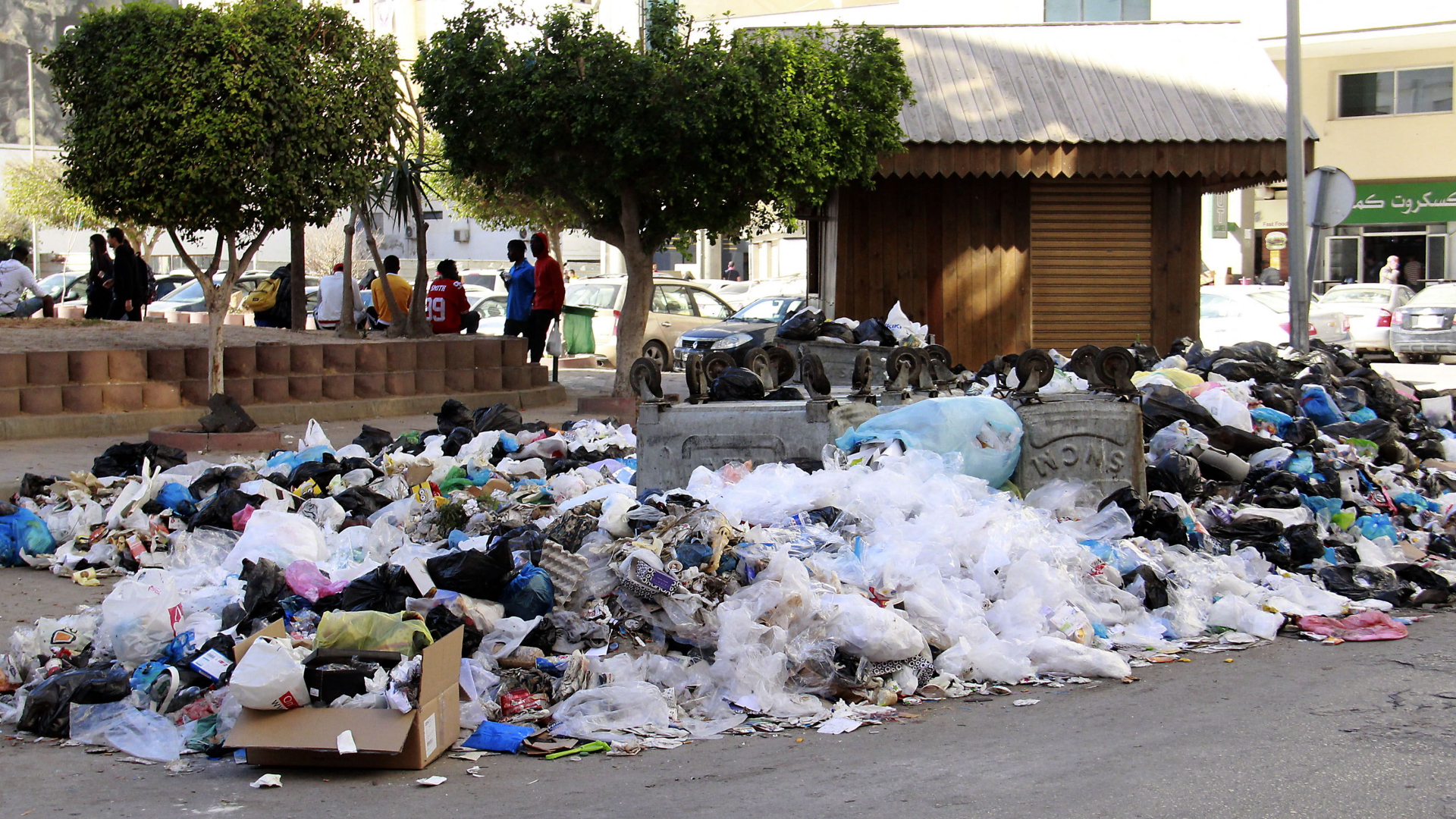 Jugendliche sitzen an einem Platz in Sfax. Im Vordergrund liegt Müll auf der Straße. | AFP