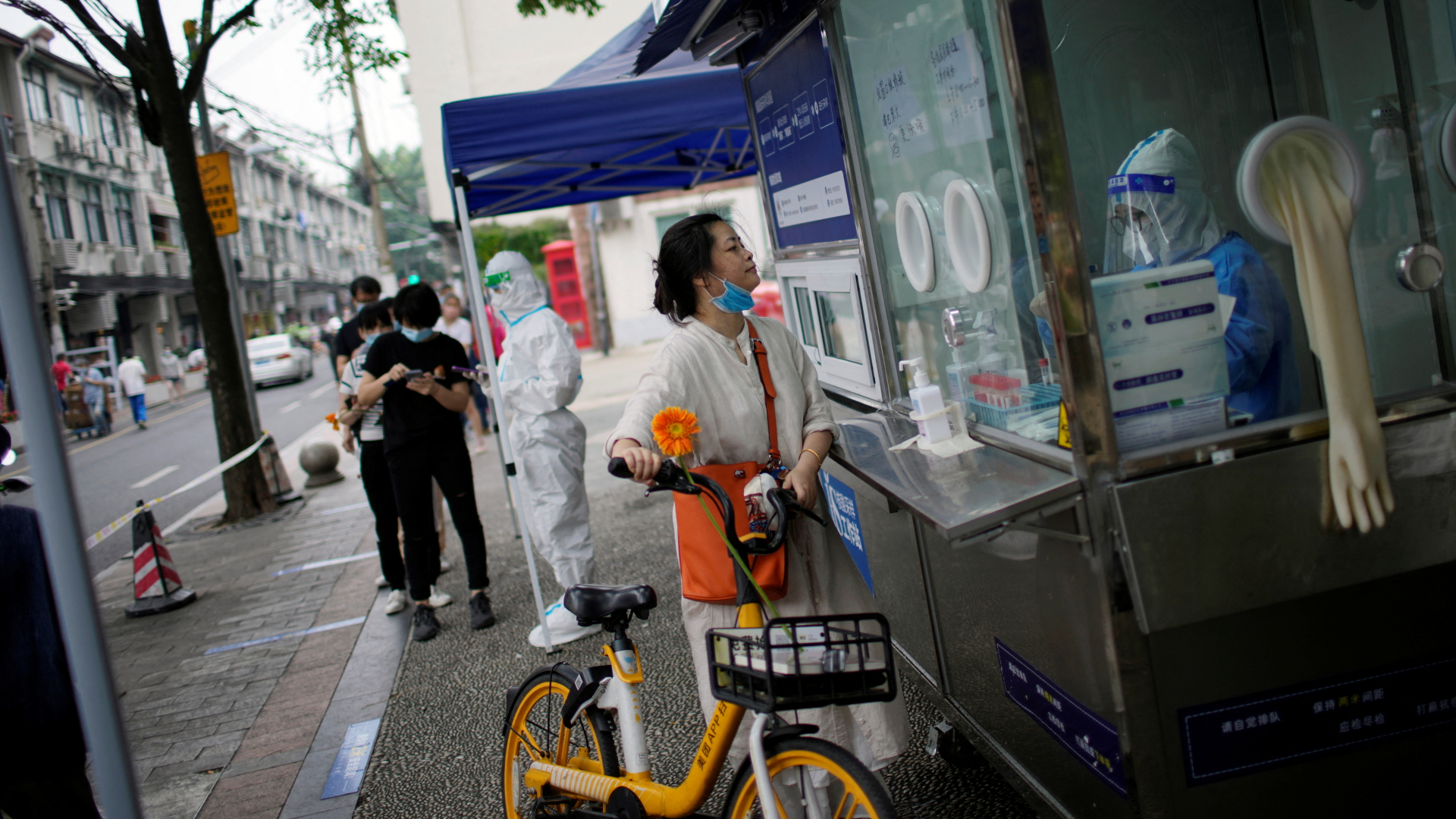 Ein Frau steht mit ihrem Fahrrad vor einer Corona-Teststation in Shanghai. | REUTERS