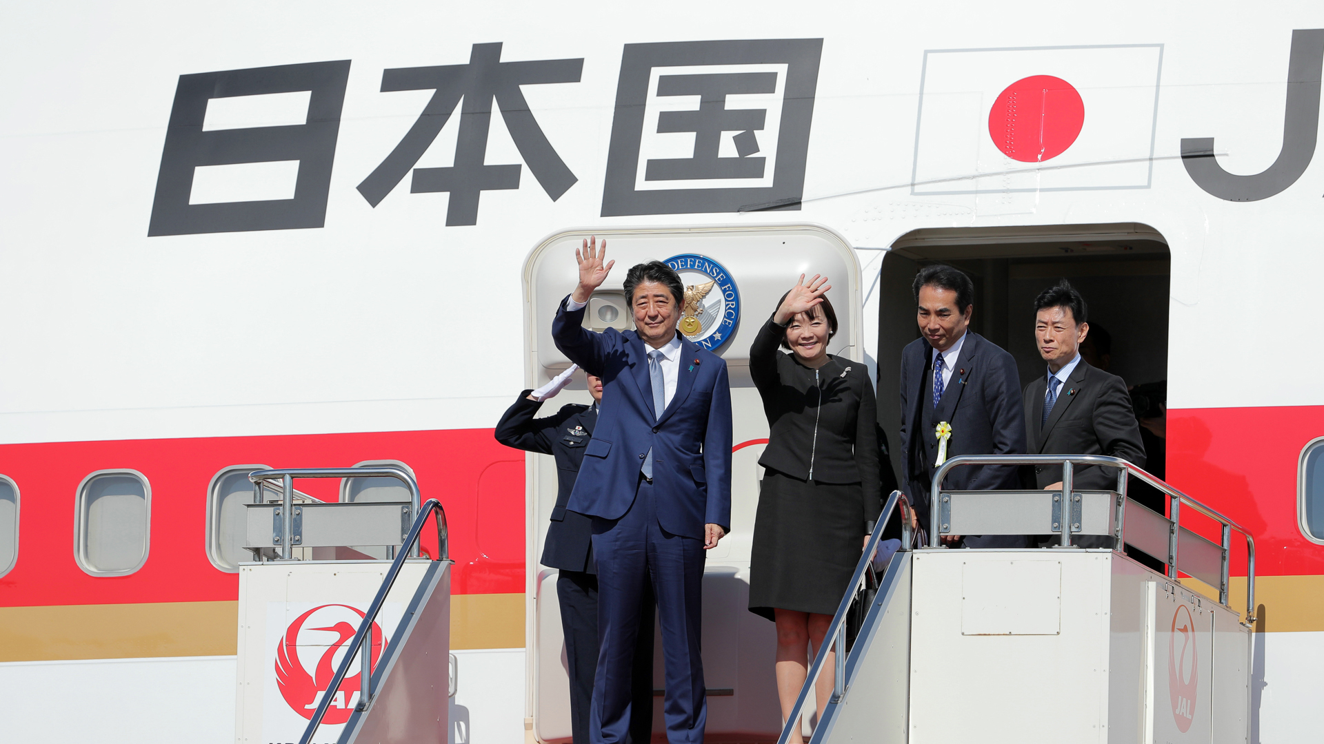 Japans Premier Abe und seine Frau Akie winken vor dem Einstieg ins Flugzeug nach Peking. | Bildquelle: picture alliance/dpa