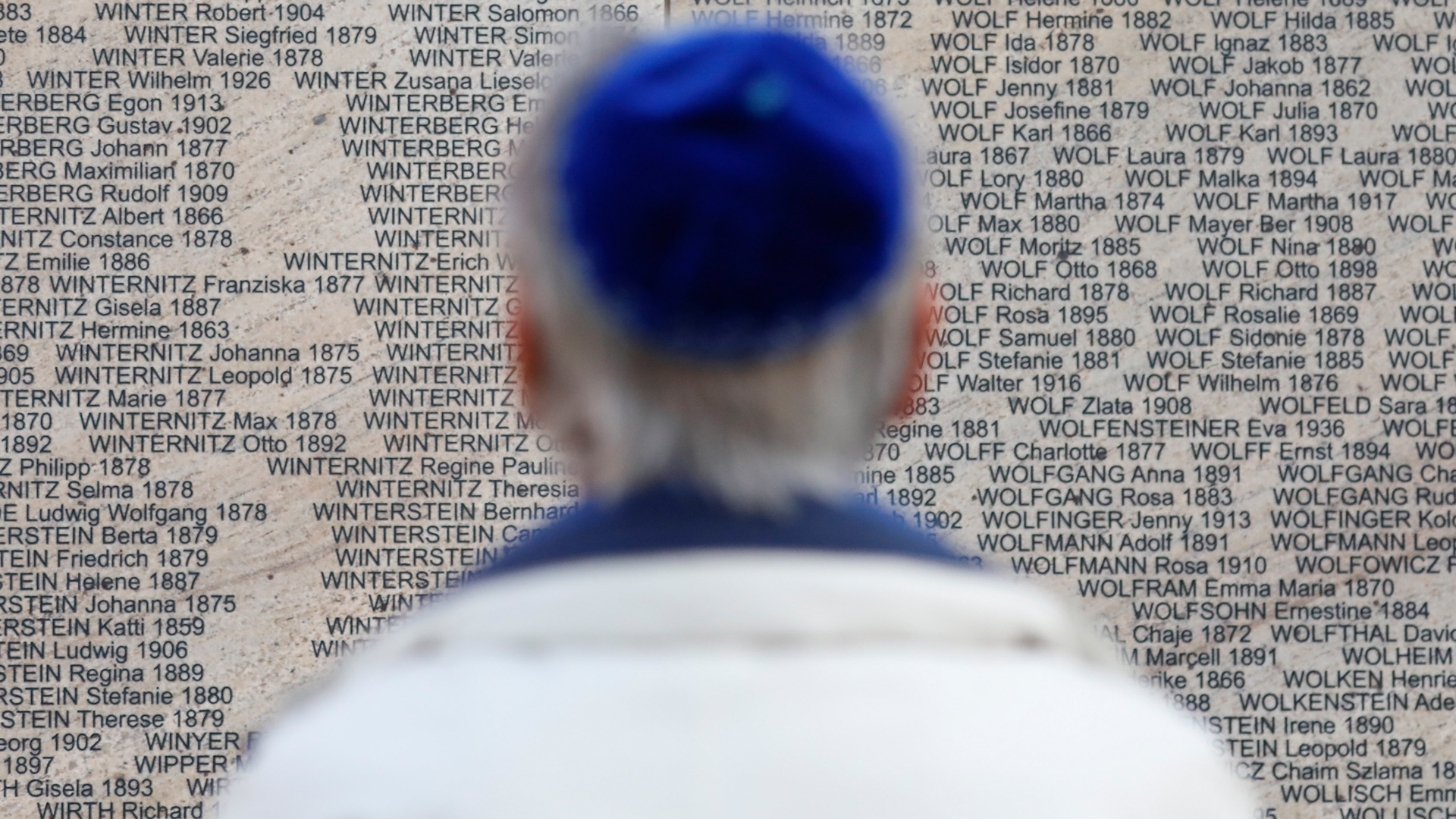 Ein Mann steht vor dem eingravierten Namen seines Großvaters an der Shoah-Gedenkmauer