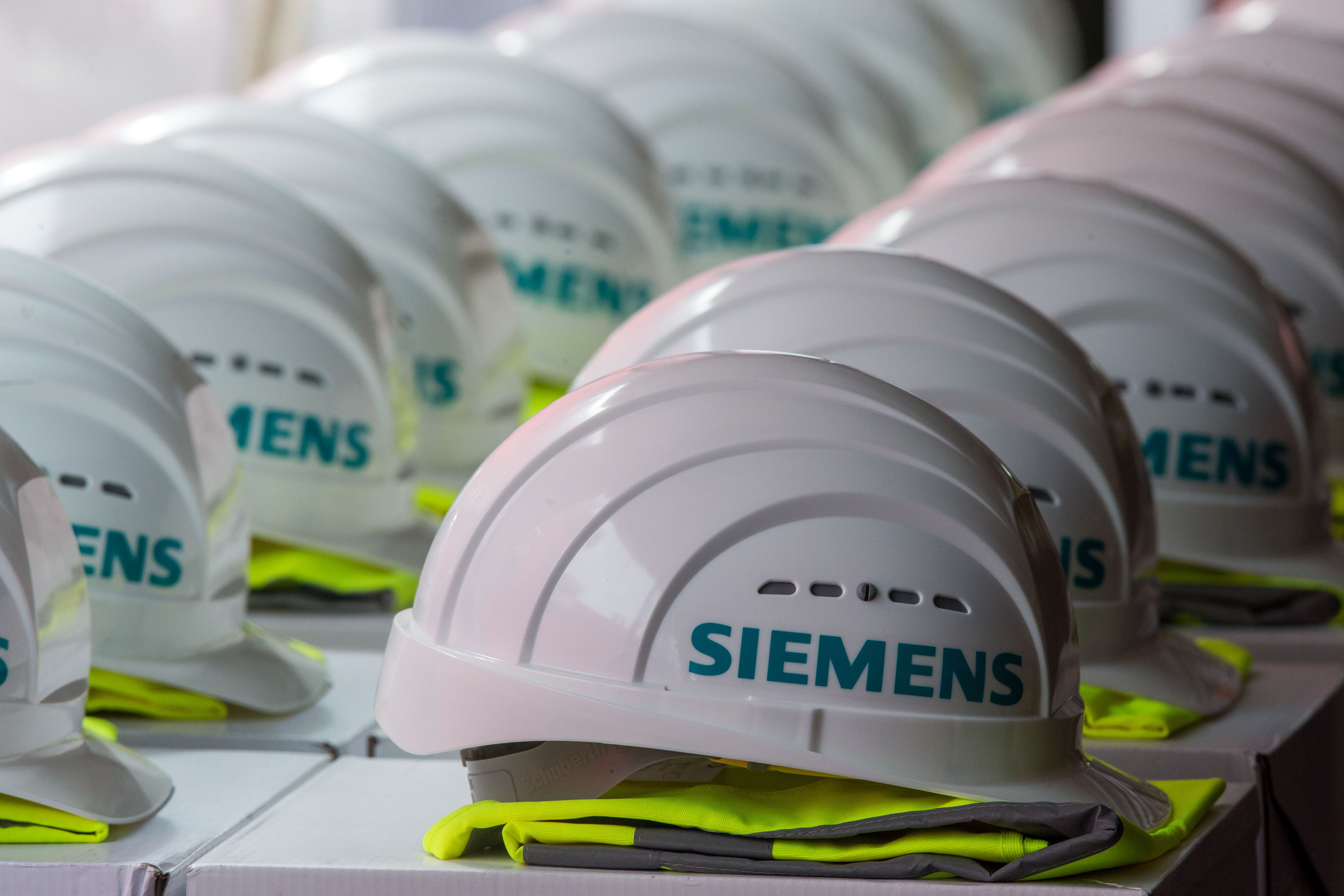 Bauhelme mit dem Logo des Siemens-Konzerns liegen auf einem langen Tisch | picture alliance / Jens Büttner/dpa-Zentralbild/dpa