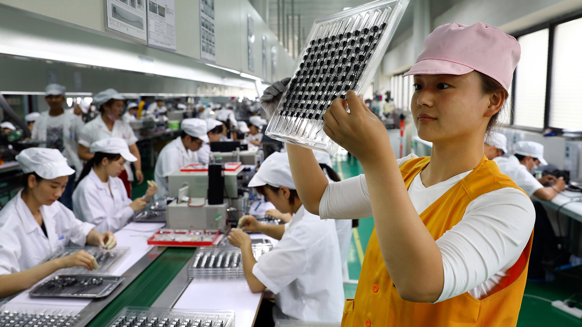 Eine Arbeiterin inspiziert die Mikromotoren für Handys in einer high-tech-Fabrik. (Archivbild) | picture alliance/dpa