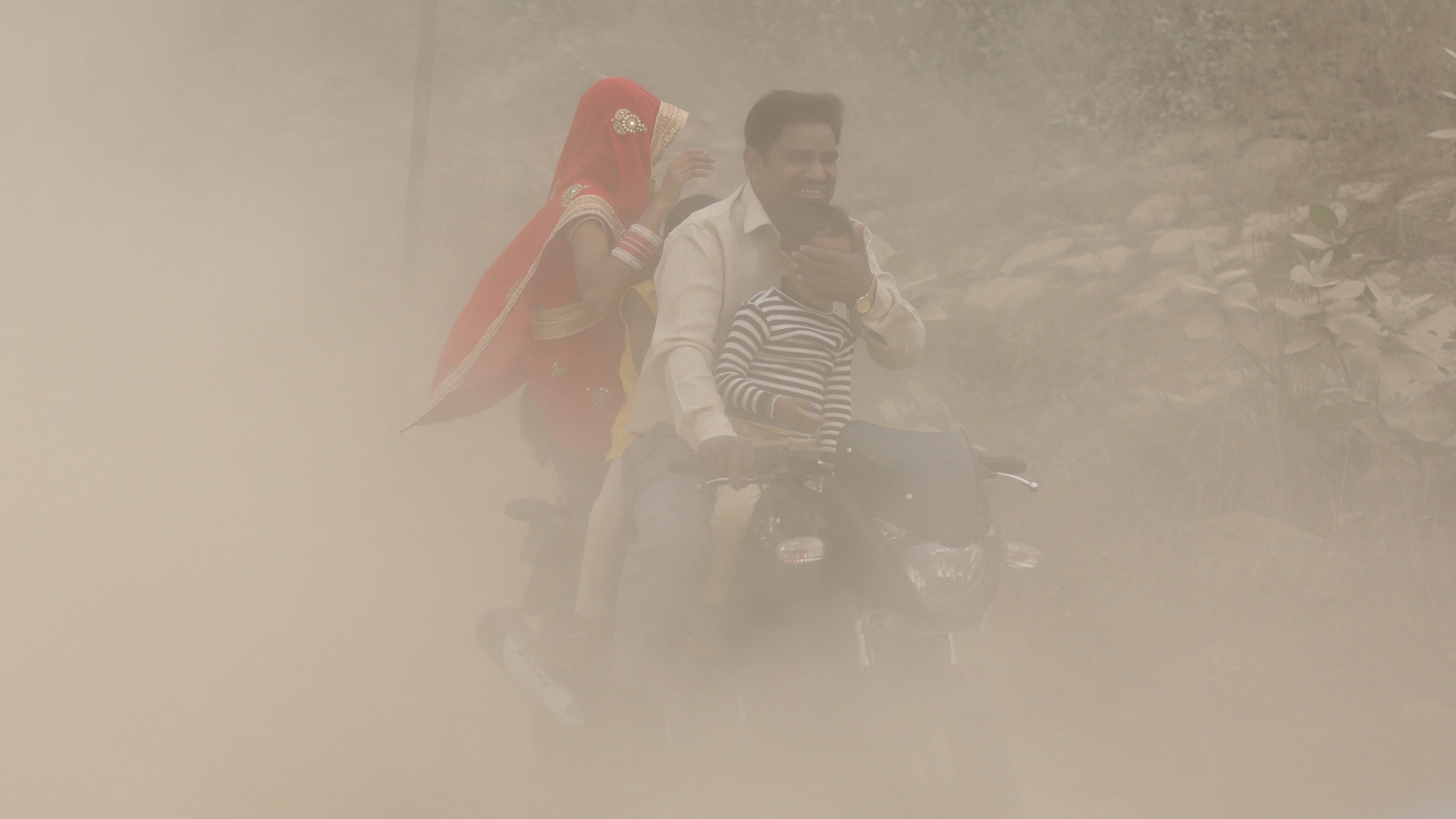 Ein Mann fährt in Neu-Delhi seine Familie auf einem Motorroller durch Smog (Archivbild vom 06.11.2016) | dpa