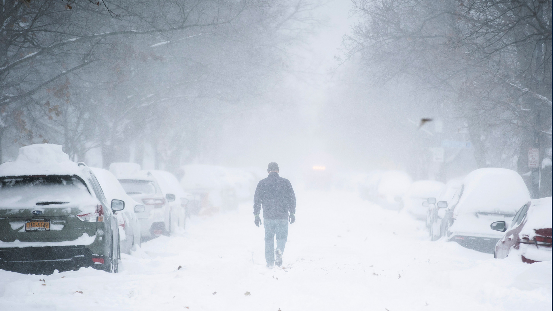 Ein Mann geht auf einer schneebedeckten Straße durch einen Schneesturm. | AP