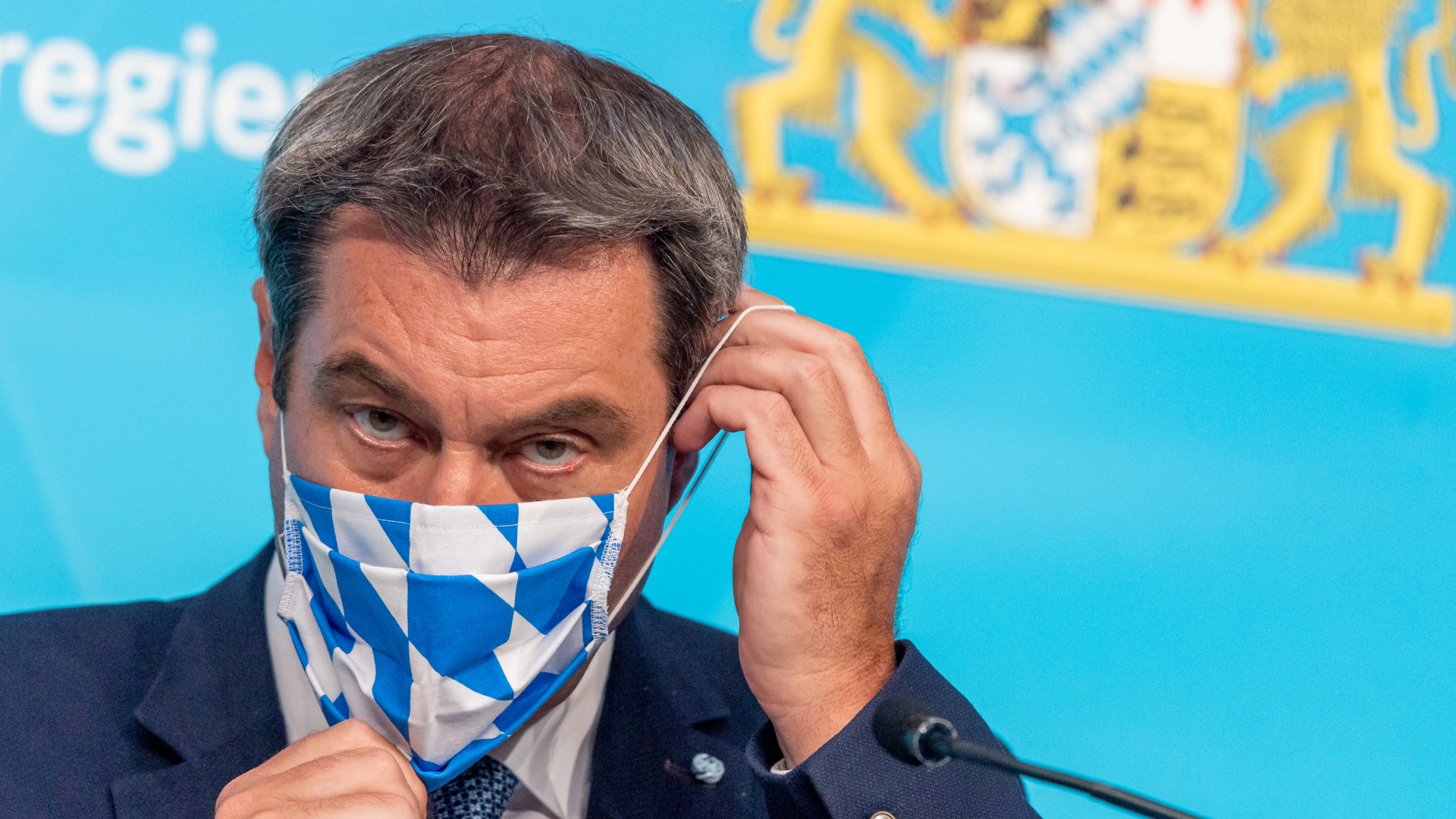 Bayerns Ministerpräsident Markus Söder zieht sich eine Schutzmaske mit bayerischem Rautenmotiv an. | Bildquelle: dpa