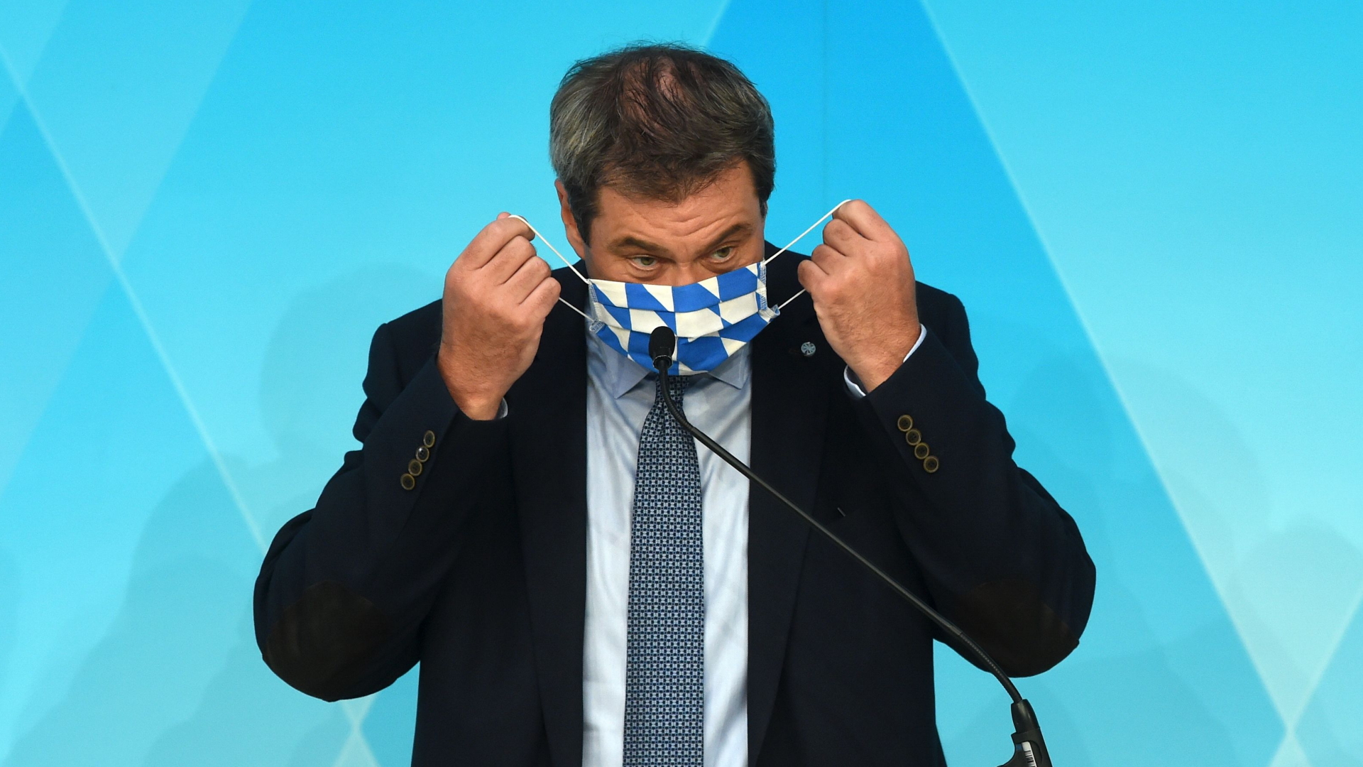 Ministerpräsident Söder nimmt einen Mundschutz in den Landesfarben ab. | AFP