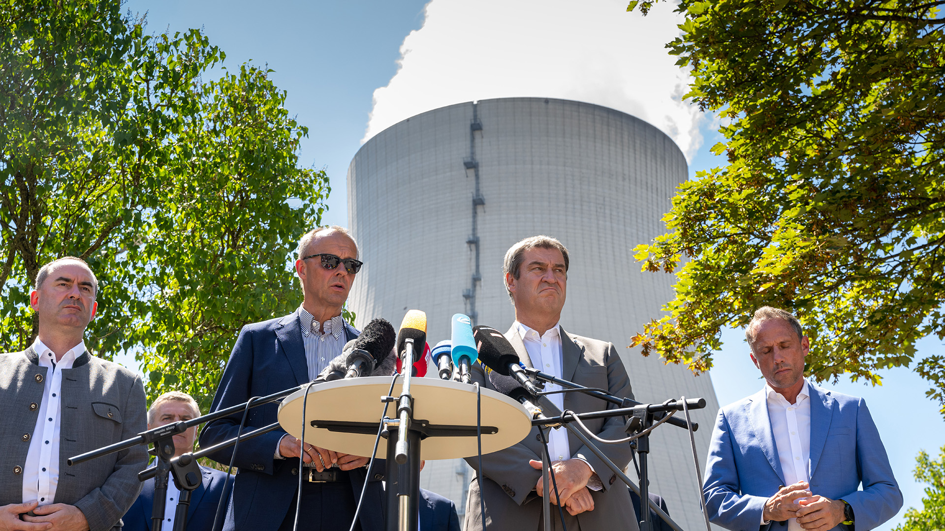 Hubert Aiwanger, Friedrich Merz, Markus Söder und Thorsten Glauber stehen vor dem Kühlturm des Kernkraftwerks Isar 2. | dpa