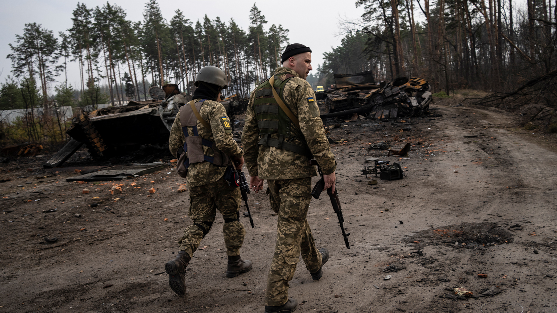 Zwei ukrainische Soldaten gehen eine Straße entlang, auf der zerstörte russische Panzer stehen. (Archivbild 31.03.2022) | dpa