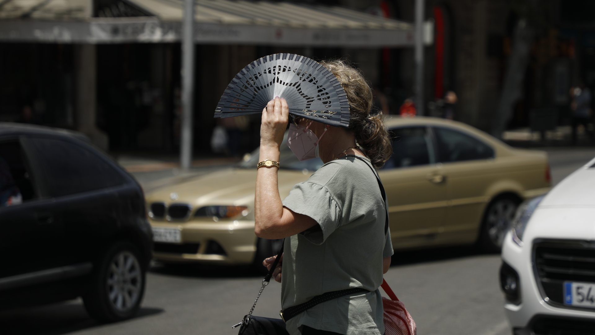 Eine Frau überquert eine Straße und bedeckt sich mit einem Fächer in Palma de Mallorca während einer Hitzewelle. Sie trägt eine FFP2-Maske. | dpa