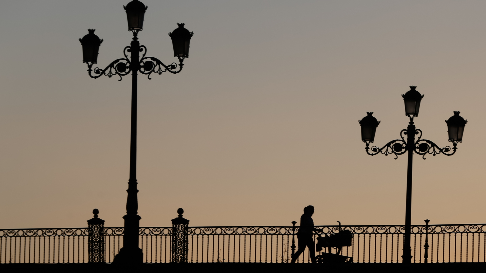 Eine Frau mit einem Kinderwagen geht beim Sonnenuntergang während der Corona-Krise über eine Brücke in Sevilla. | dpa