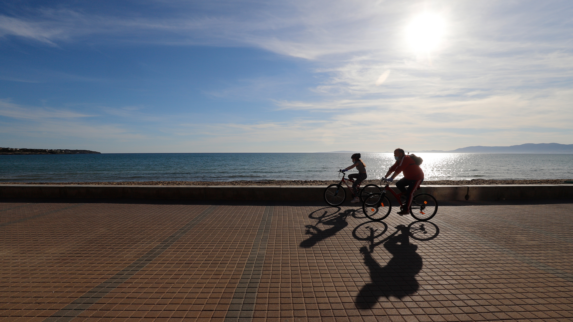 Zwei Radfahrer fahren auf der Promenade am Strand El Arenal in Palma de Mallorca entlang. | dpa