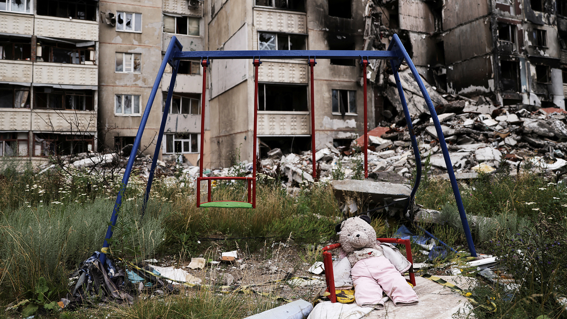 Ein Teddybär sitzt neben einer Schaukel auf einem vom Krieg zerstörten Spielplatz. | REUTERS