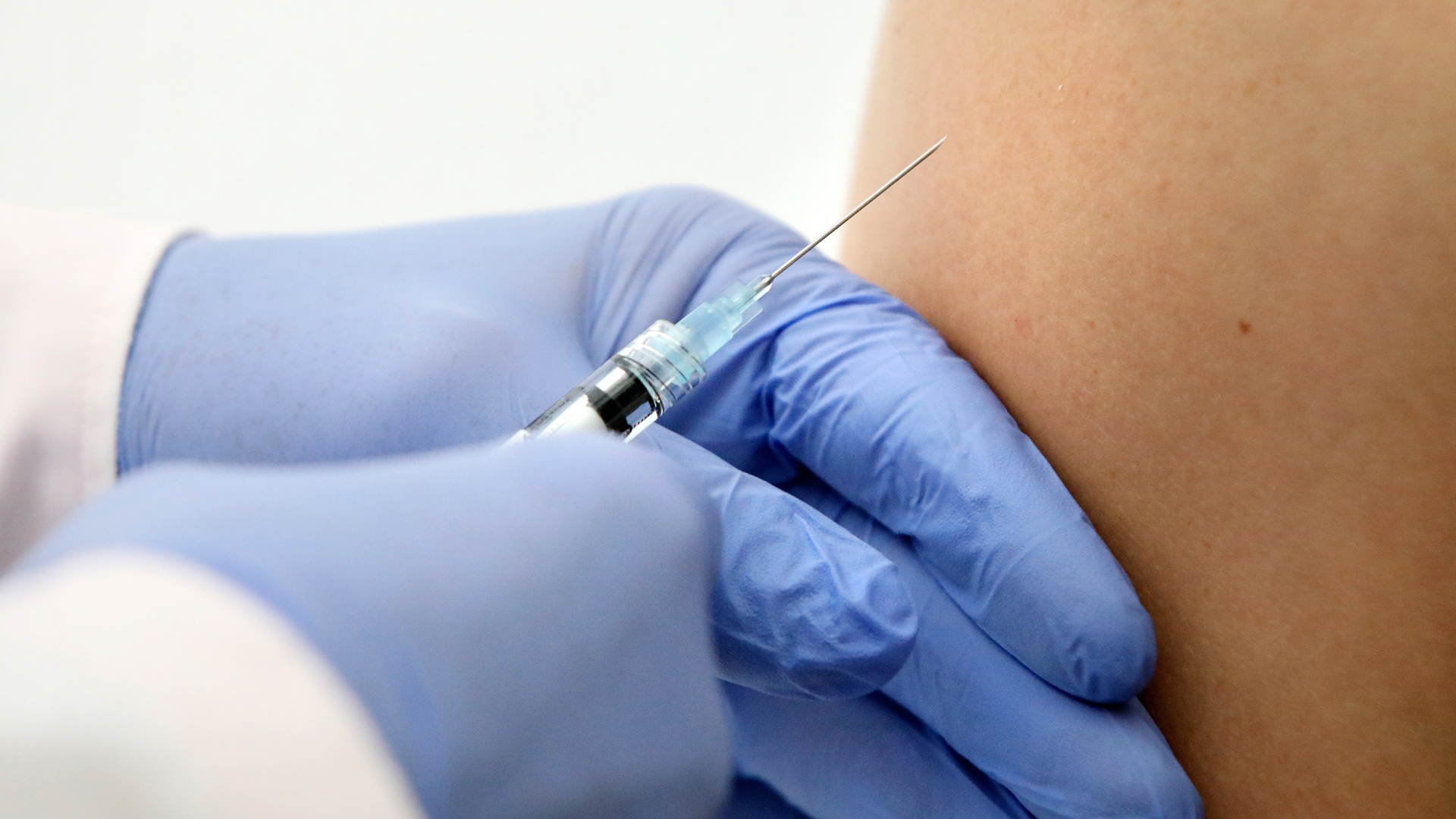 Ein Hand mit blauem Handschuh hält eine Spritze mit einem Impfstoff