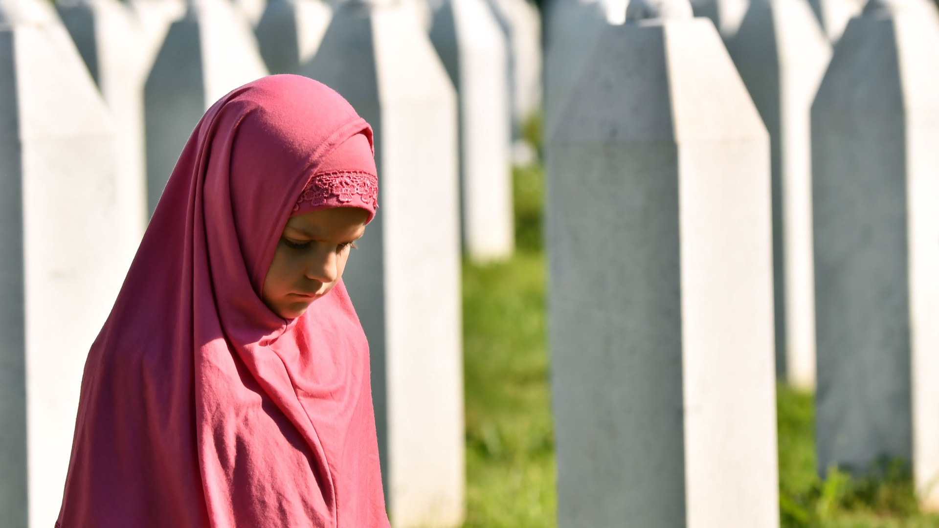 Ein bosnisches Mädchen geht mit gesenktem Kopf an Grabsteinen in Srebrenica-Potocari entlang | AFP