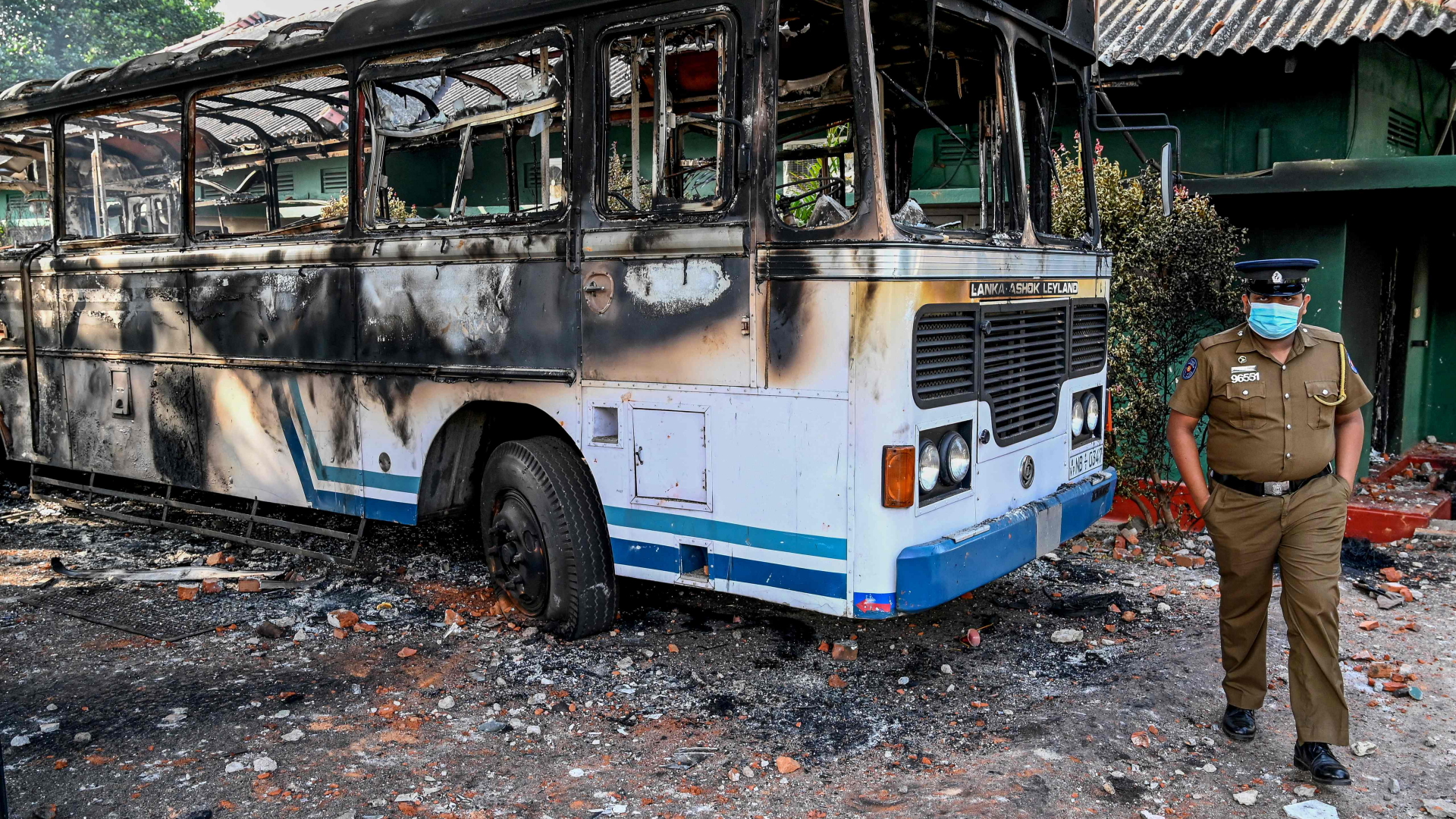 Ein Polizist steht vor einem ausgebrannten Bus in Sri Lanka | AFP