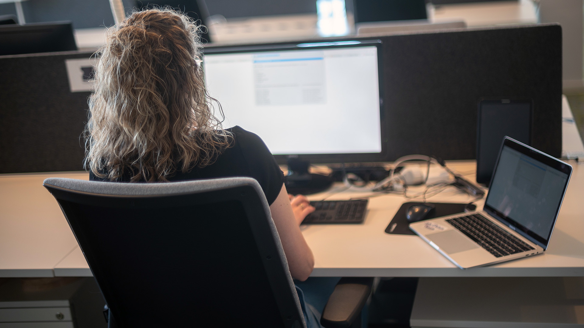 Eine Frau sitzt an einem Arbeitsplatz mit Bildschirm und Laptop. | picture alliance/dpa