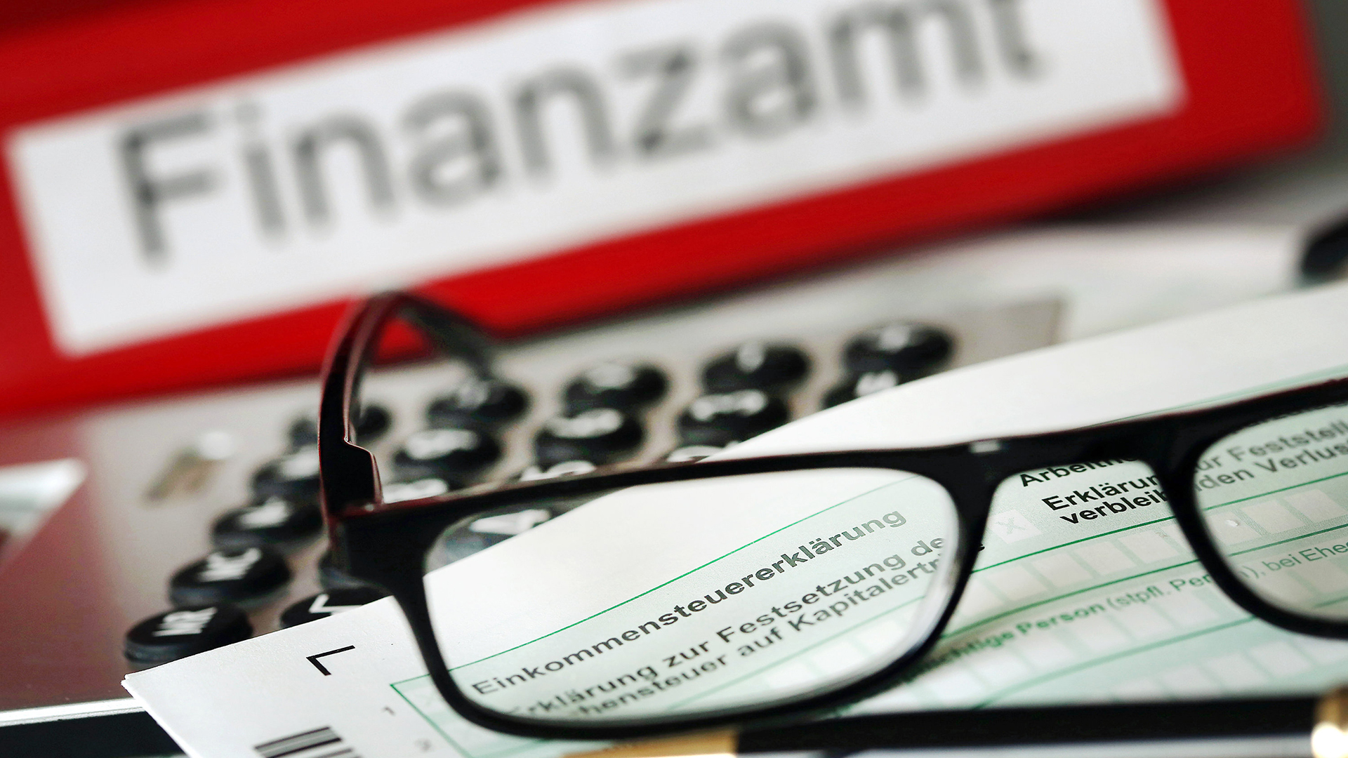 Auf einem Vordruck für die Steuererklärung liegt vor dem Aktenordner mit dem Aufdruck "Finanzamt" ein Stift und eine Brille.  | dpa