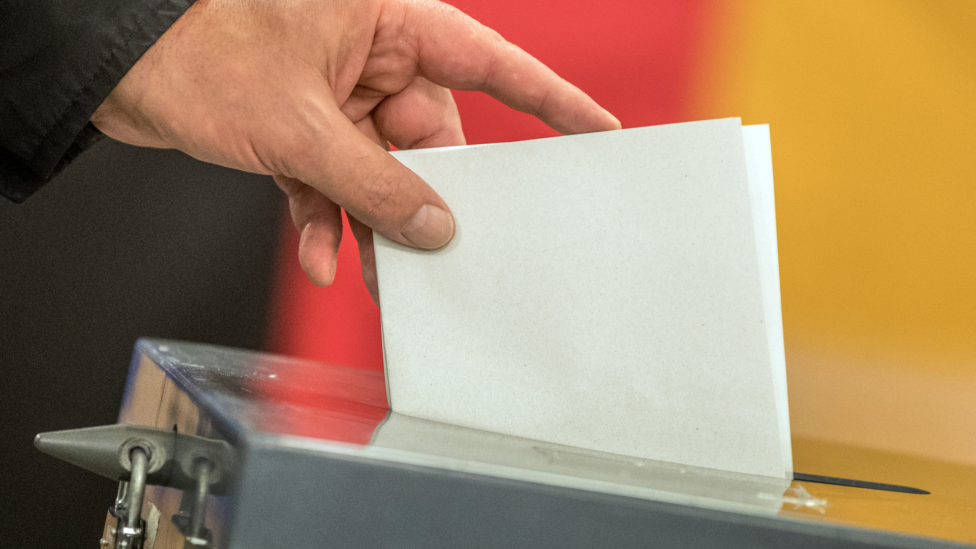 Hand steckt Zettel in Wahlurne | dpa