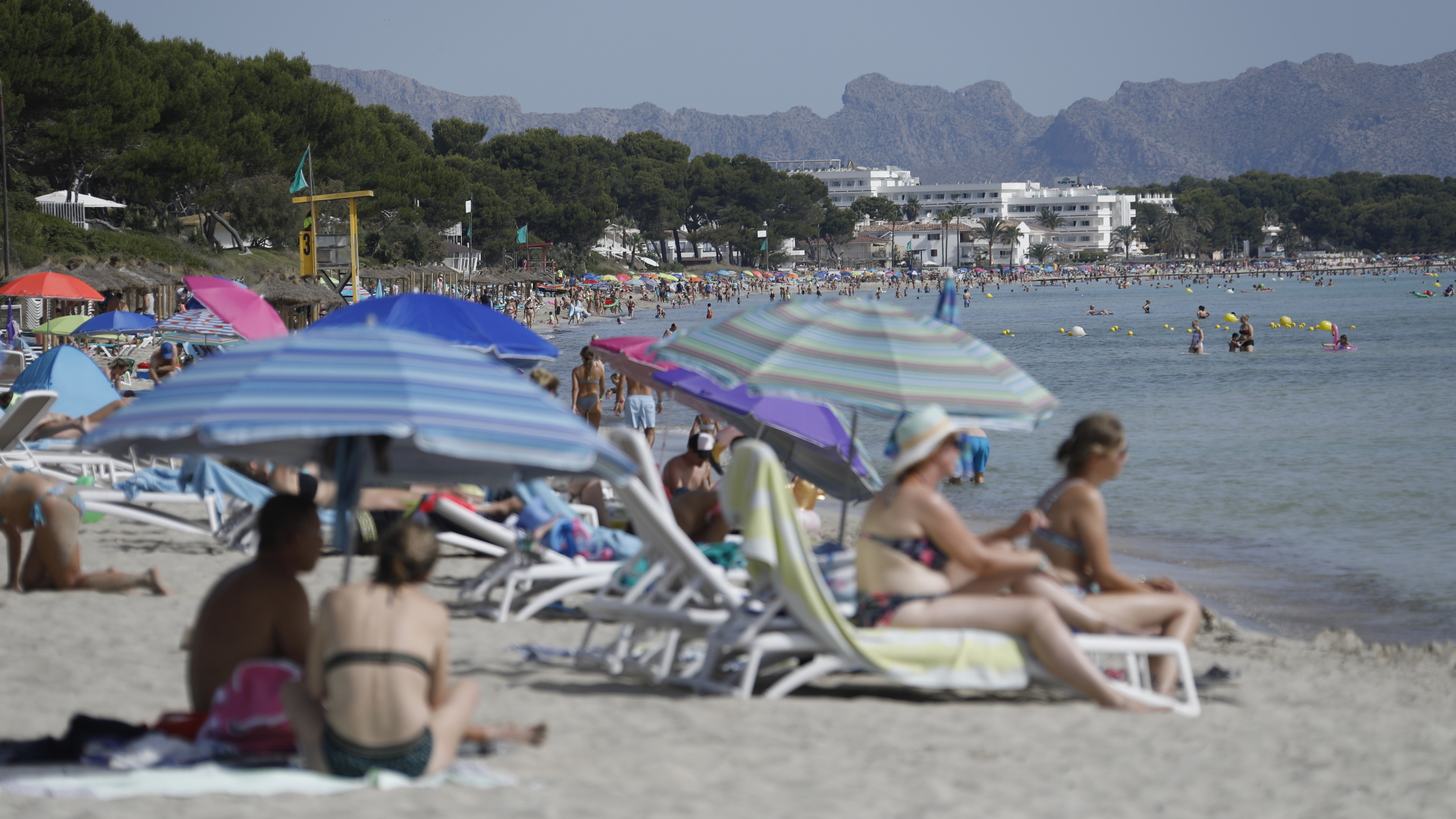 Menschen sitzen am Strand Playa de Muro auf Mallorca. | dpa