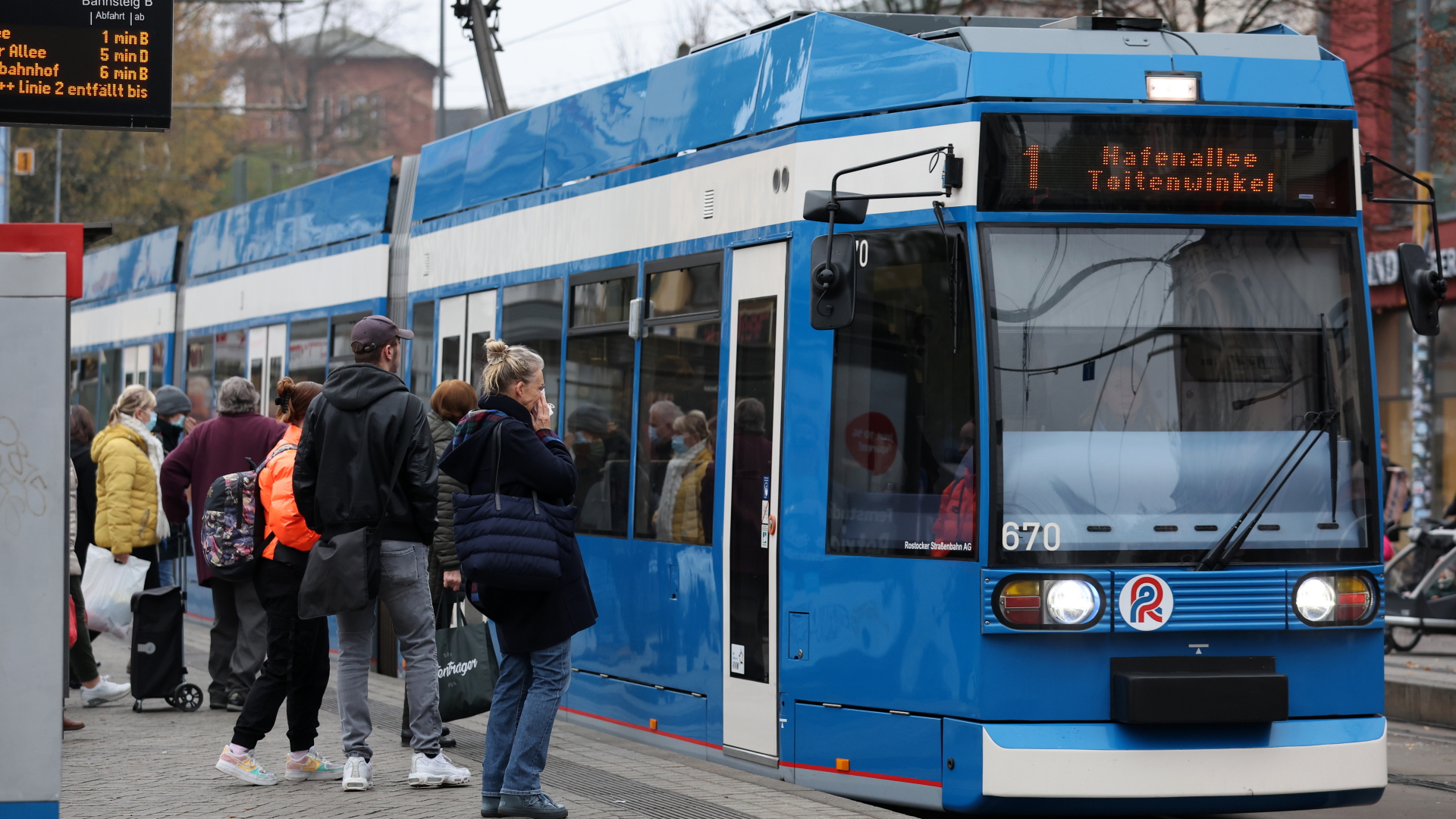 Fahrgäste stehen in Rostock vor einer einfahrenden Straßenbahn.