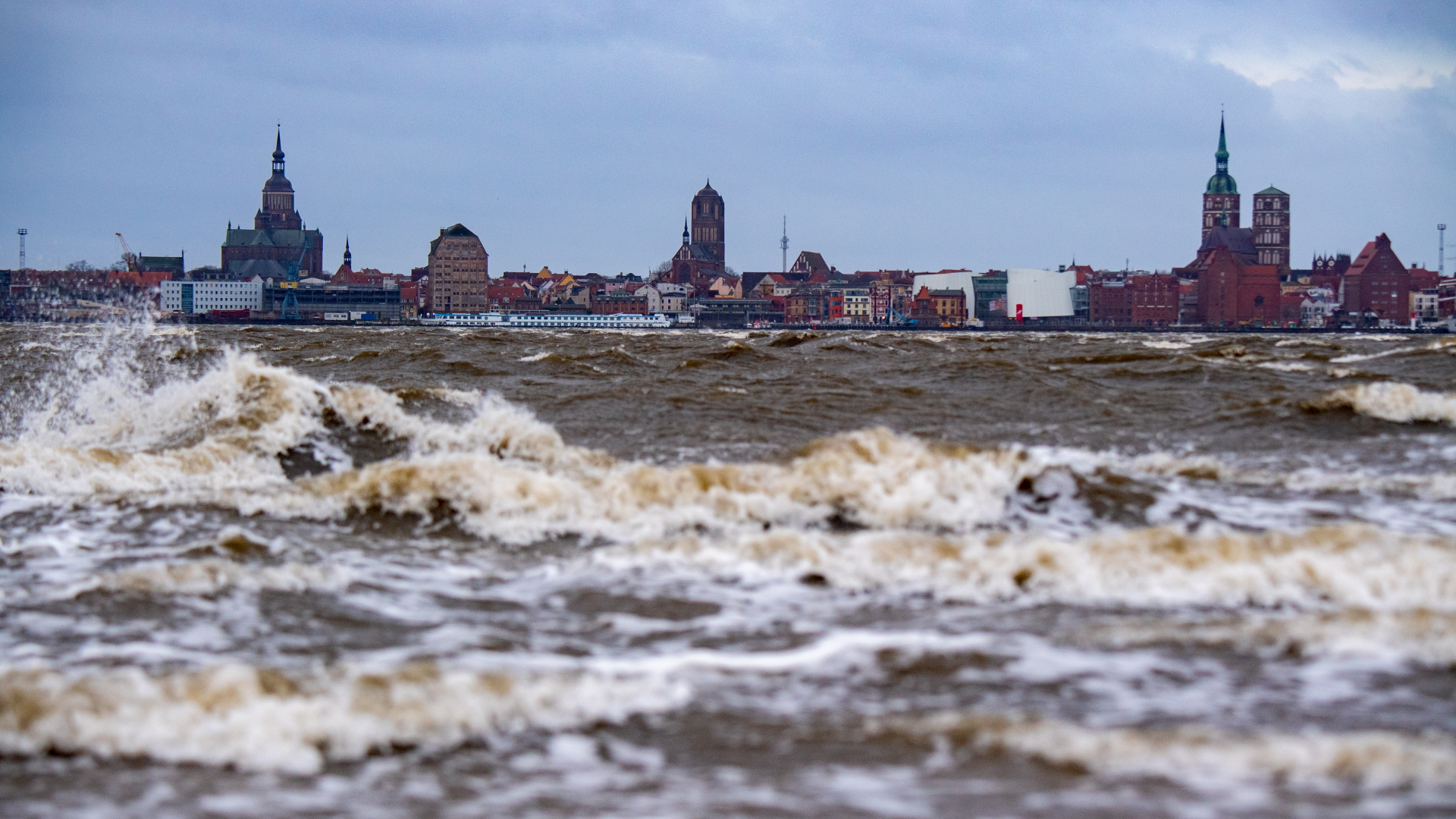Wellen brechen sich am Strand von Altefähr auf der Insel Rügen. Im Hintergrund ist die Silhouette der Hansestadt Stralsund zu sehen.  | dpa