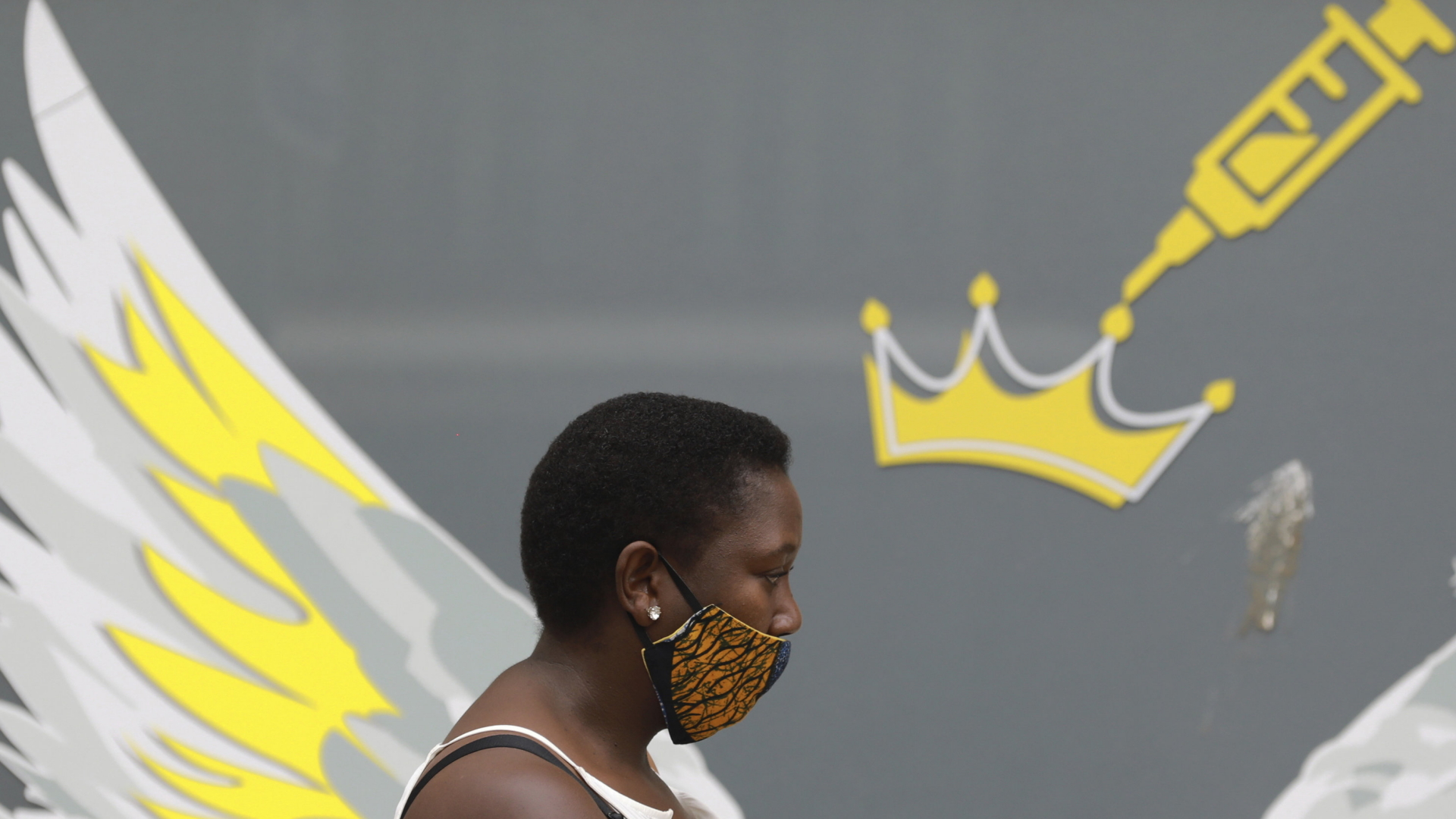 Frau in Kapstadt geht mit Mundschutz an einem Graffiti mit Injektionsspritze vorbei