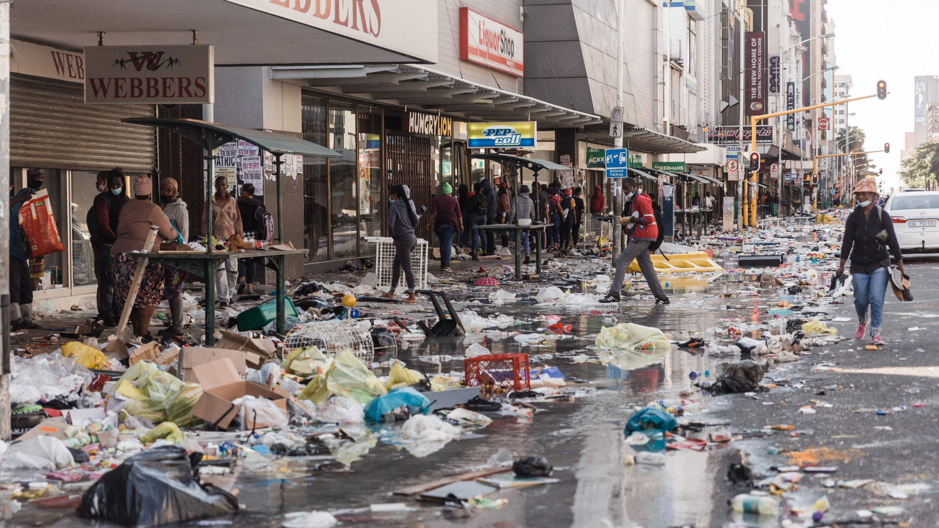 Menschen laufen an den bei Protesten im südafrikanischen Durban geplünderten Läden vorbei. | AFP