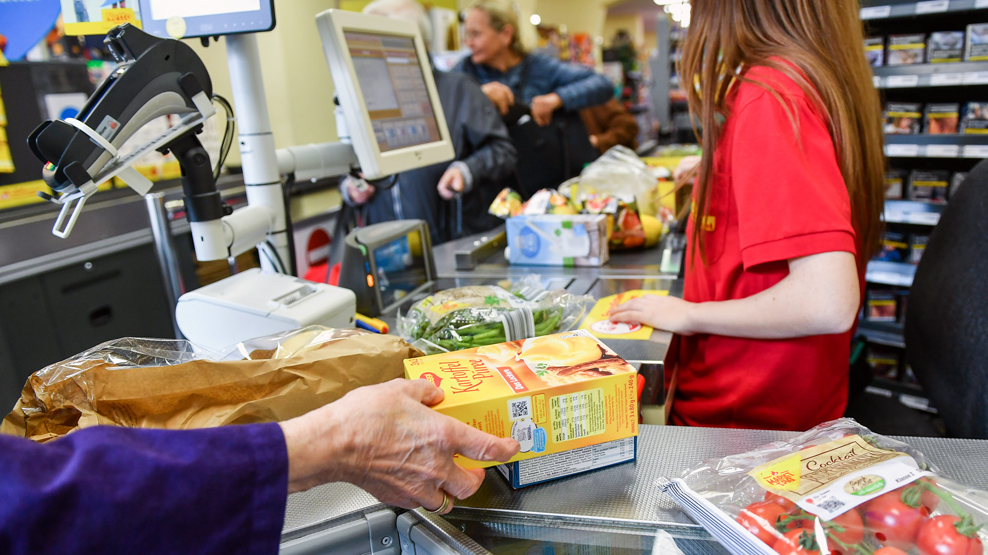 Eine Kundin nimmt in einem Berliner Supermarkt Waren vom Band an der Kasse, nachdem eine Kassiererin die Waren gescannt hat.  | dpa