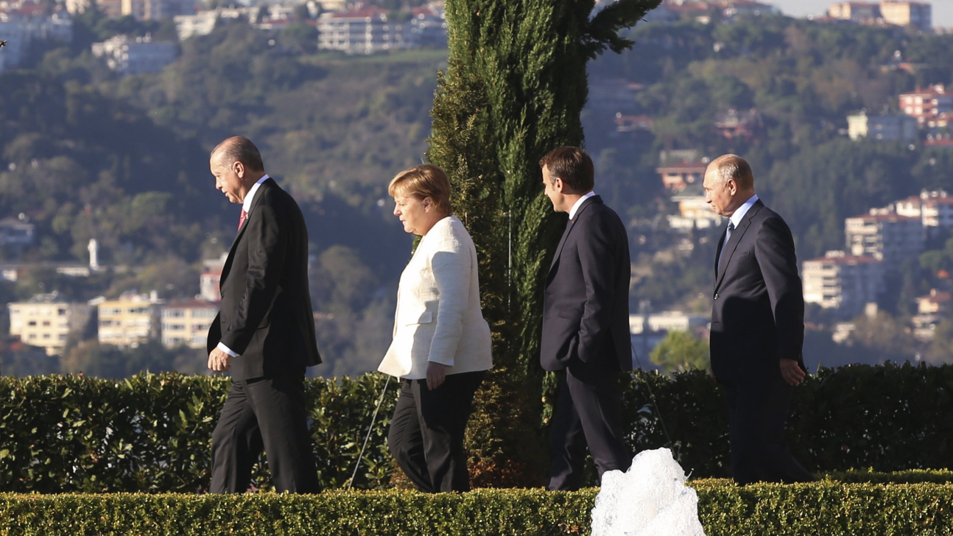 Der türkische Präsident Erdogan (von links), Kanzlerin Merkel, Frankreichs Präsident Macron und der russische Staatschef Putin laufen in einer Reihe durch einen Garten in Istanbul. | Bildquelle: AP