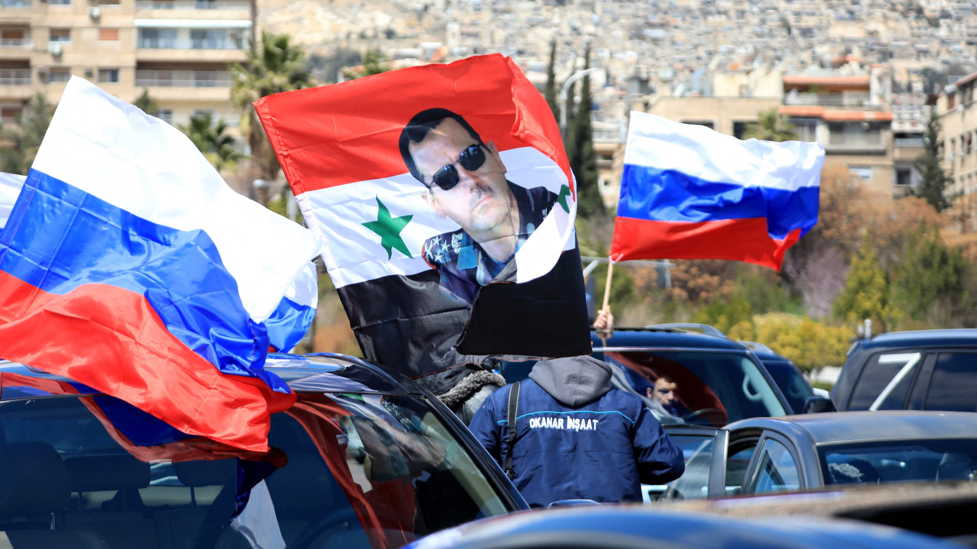 Russische Flaggen und Syriens Machthaber Baschar Al-Assad auf einer Kundgebung in Damaskus. | AFP