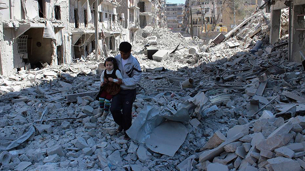Ein Mann trägt ein kleines Mädchen durch eine zerbombte Straße in Aleppo.