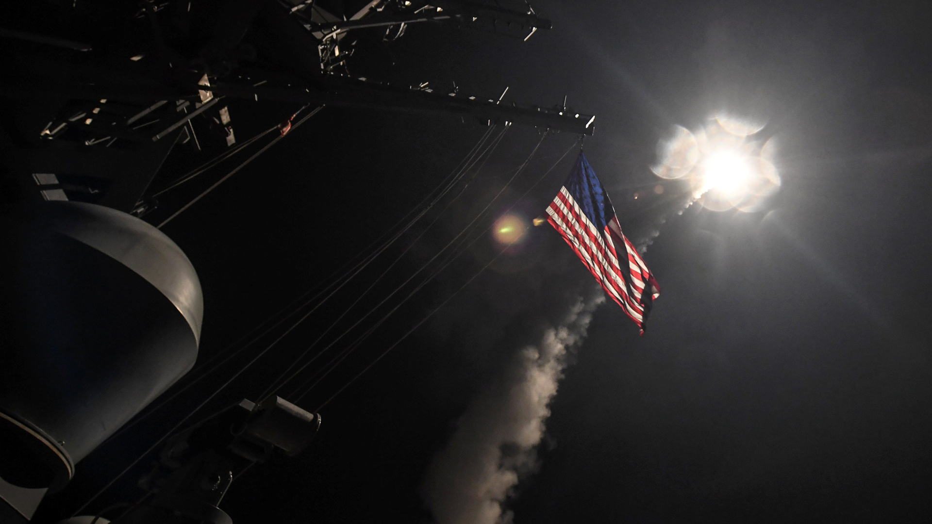 Vor einem dunklen Himmel über einem Schiff ist die amerikanische Flagge und eine Explosion zu sehen.