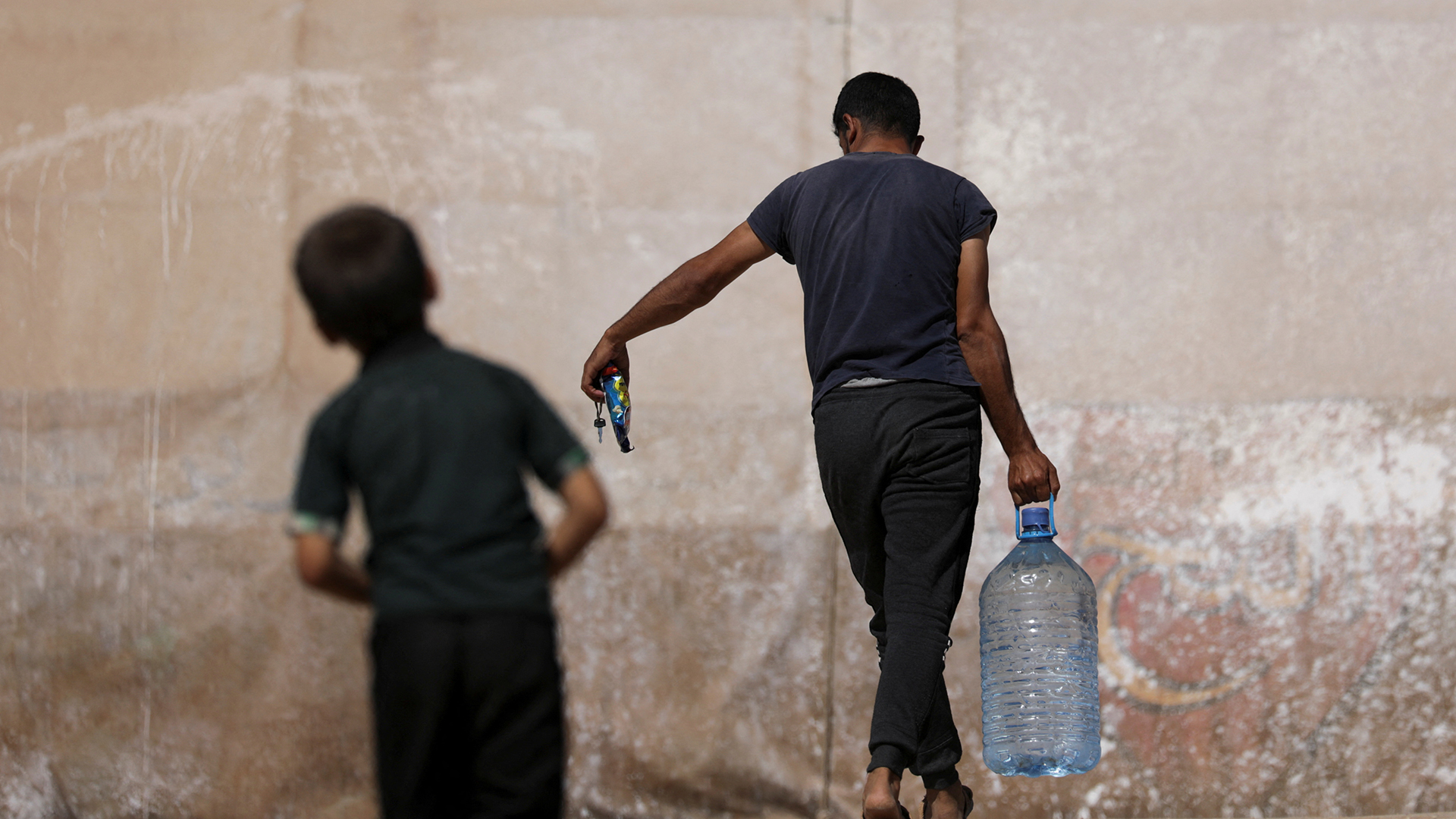 Ein Mann trägt einen großen Plastikbehälter mit Wasser. | REUTERS