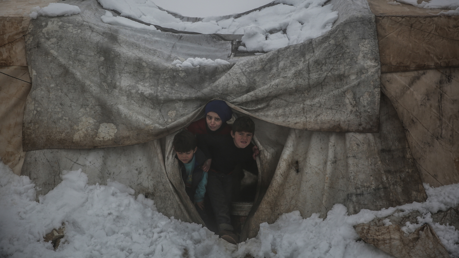 Geflüchtete Kinder schauen aus einem verschneiten Zelt hervor. | dpa
