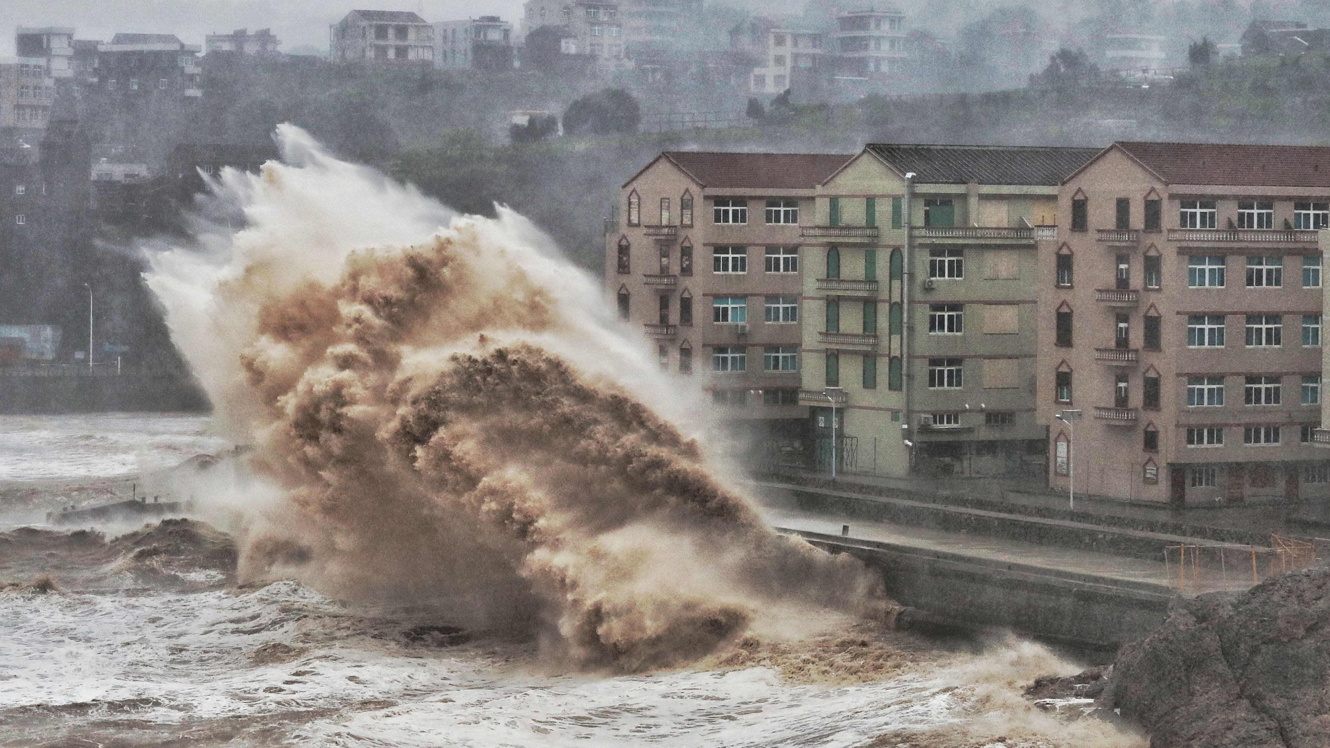 Eine hohe Welle rollt auf zwei Wohnhäuser in Taizhou in der östlichen Zhejiang-Provinz in China zu. | AFP